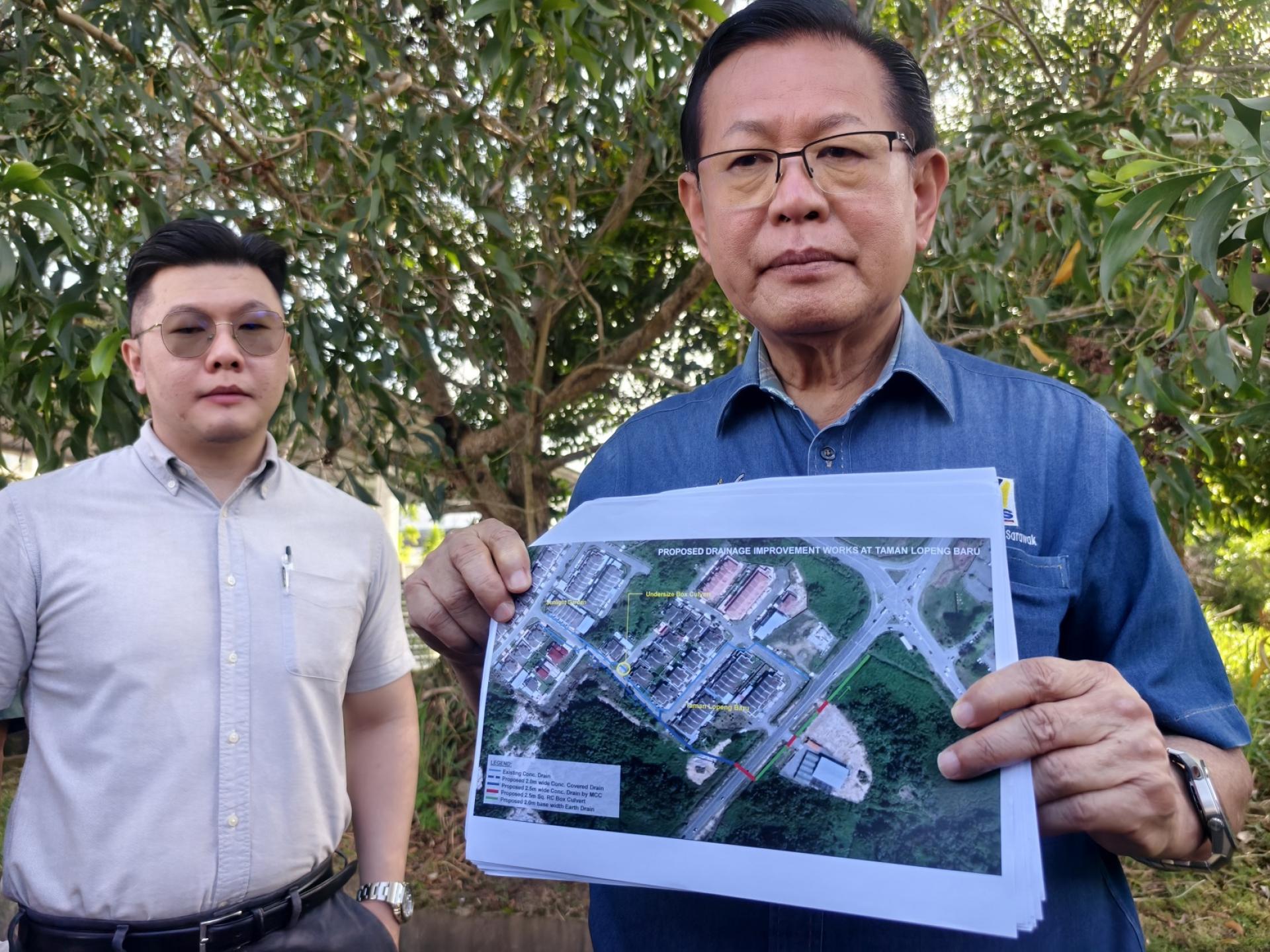 砂交通部长拿督斯里李景胜展示新罗冰花园拟建排水改善工程位置图。左为一同实地巡视的美  里水利灌溉局局长曾俊运。