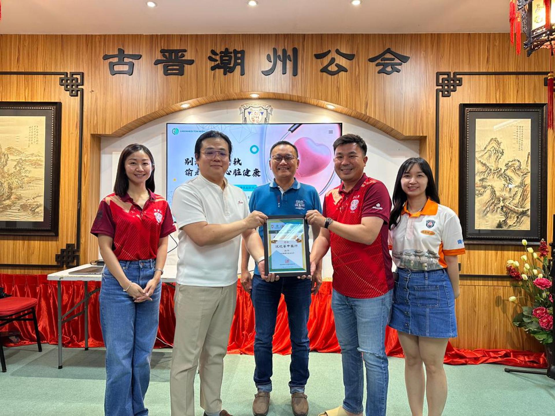 在古晋潮州公会会长陈家福（中）见证下，该会青年团团长郑元漳（右2）移交感谢状予马来西亚中医总会副总会长沈观蔷中医师（左2）。左1为青年团康乐组组长黄盈盈及青年团康乐组副组长吴慧珠（右1）。