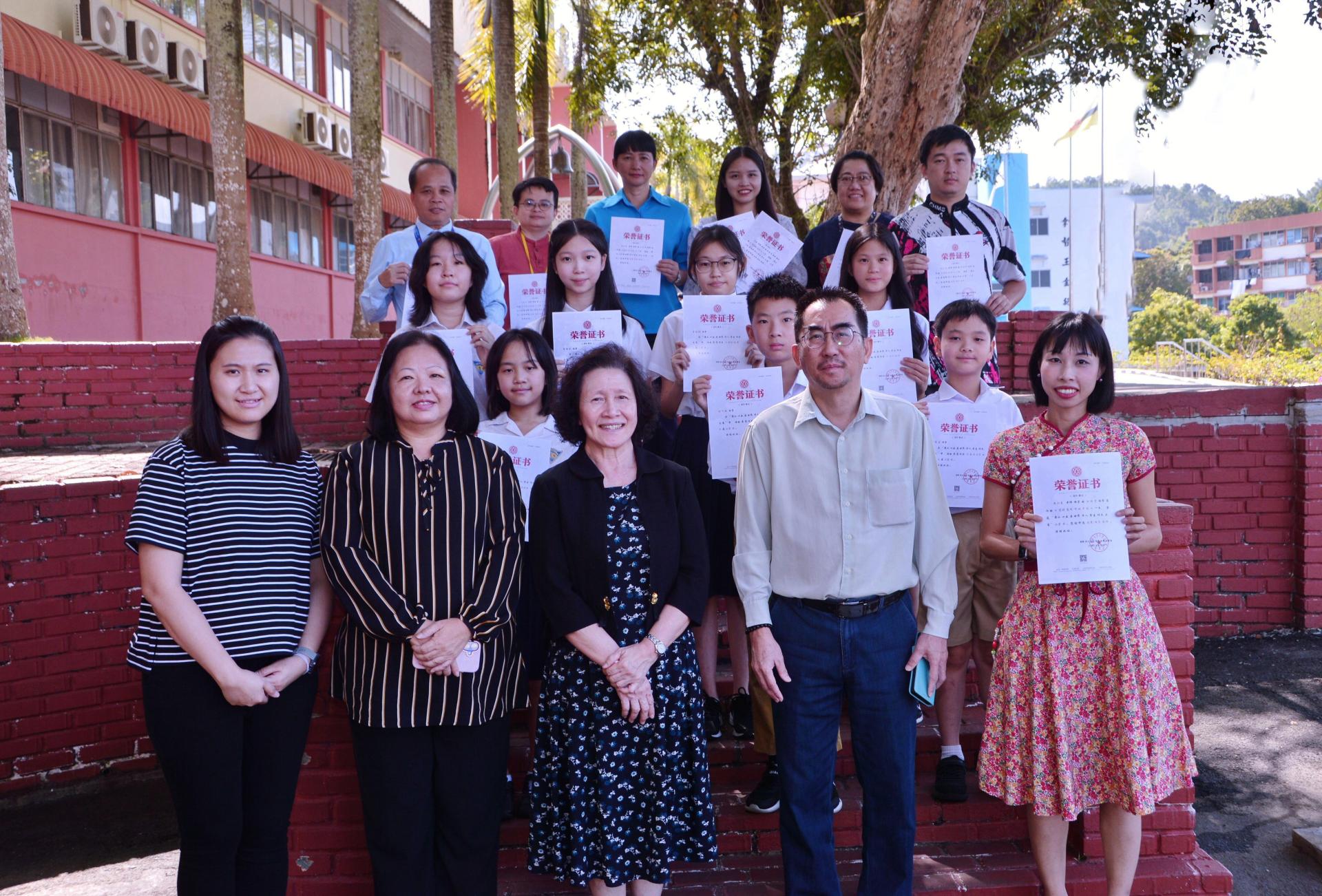 图为在第二十五届世界华人学生作文大赛中获奖的汶中师生与与许月兰校长（前中）、马海耀副校长（前右2）、陈美典助理校长（前左2）及代助理校长杜岫颖（前左）等合影。前右为华文部门主任邓巧琳；后排左起以次为优秀指导老师张清赋、贝荣彩、黄仁美、马迪、符玉华及康元僖。