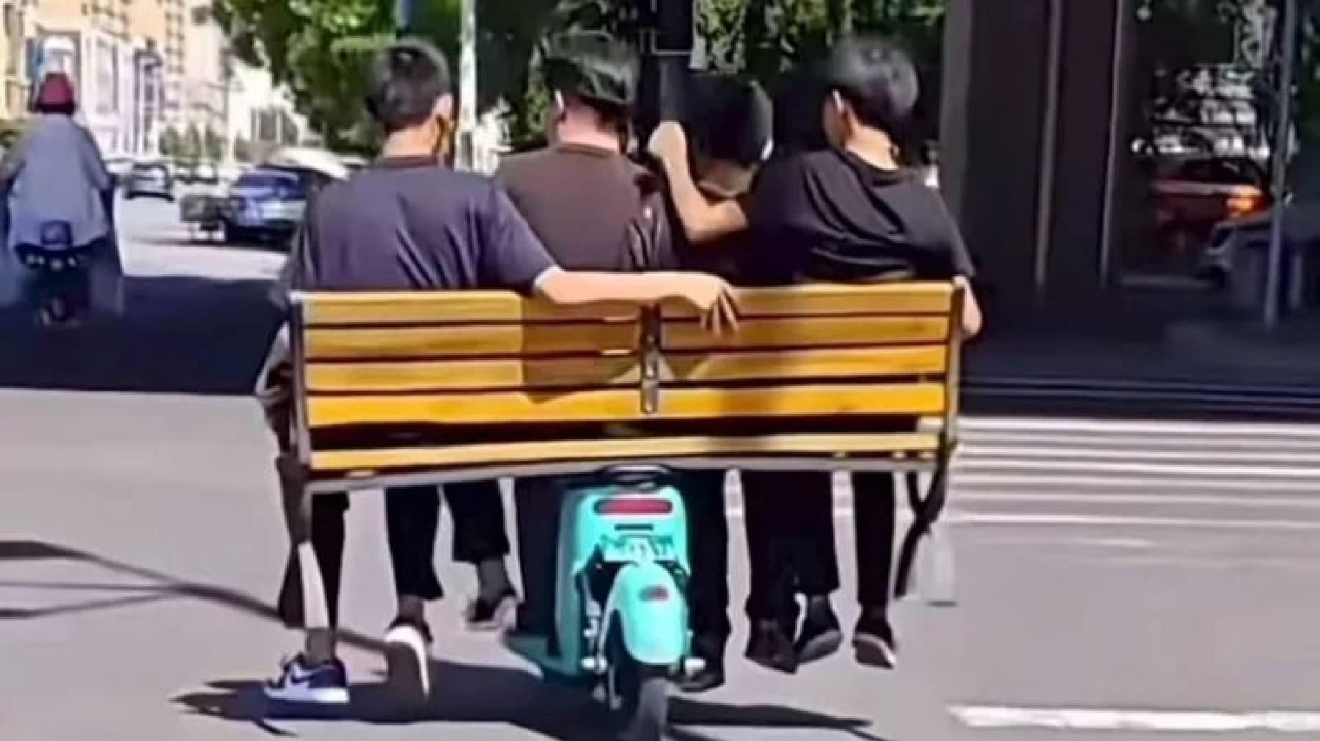 有4名少年将公园长椅横置在共享电动脚车上，他们还会逻辑性地根据体重安排座位保持平衡，但还是摇摇晃晃地在马路中间骑行。
