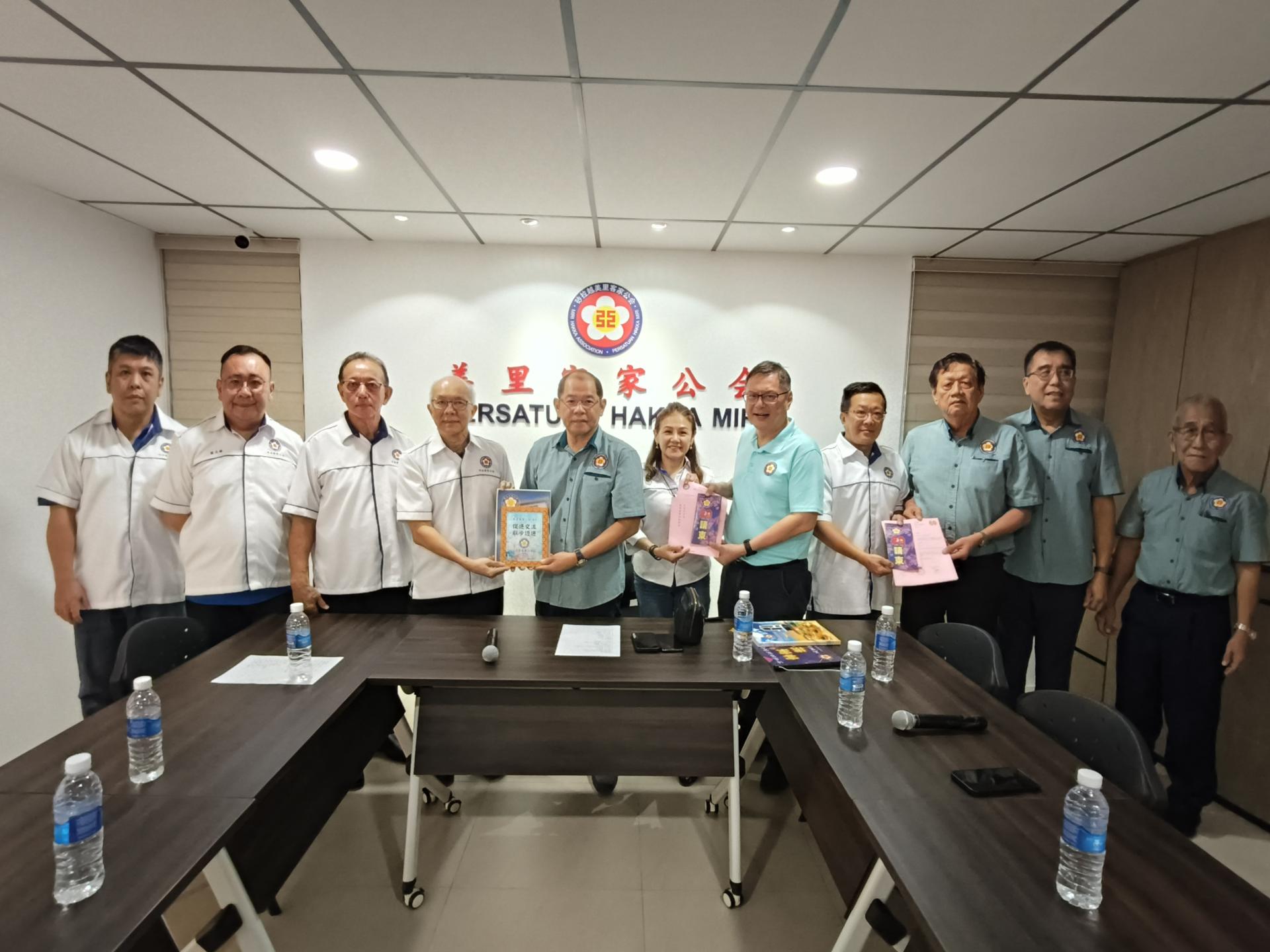 诗巫客家公会会长兼80周年庆典大会主席黄志光（左4）、诗巫客家公会80周年庆典筹备会主席蓝缨绯（中者）、及诗巫客家公会全砂客家歌邀请赛筹备会主席谢永清（右4）移交纪念品及邀请函予美里客家公会主席江先柱、美里客家公会副会长江山河及美里客家公会副主席黄能喜。
