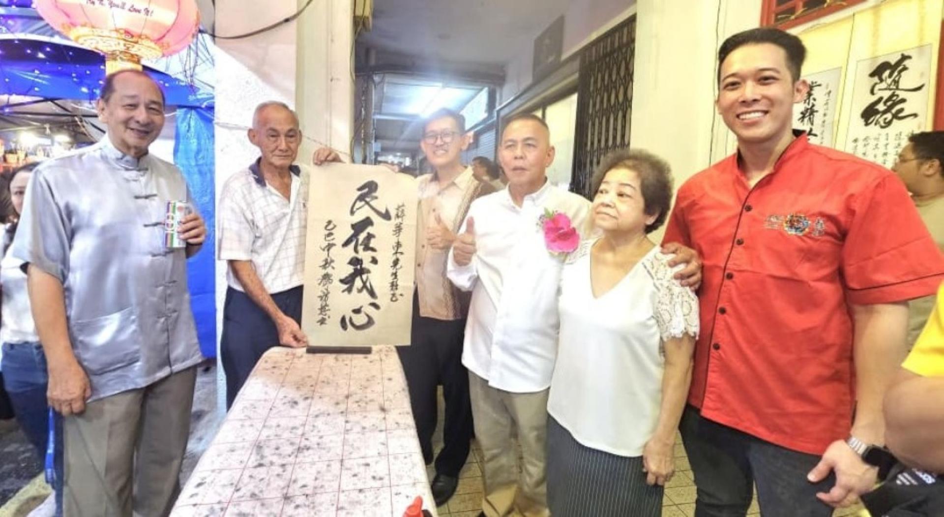 书画家邓访慈（左2）赠其墨宝“民在我心”予“文化缤纷庆中秋”顾问薛华东。右起为筹委陈柏䤵、大会会长甲必丹林传政伉俪，左为秘书孙守生。
