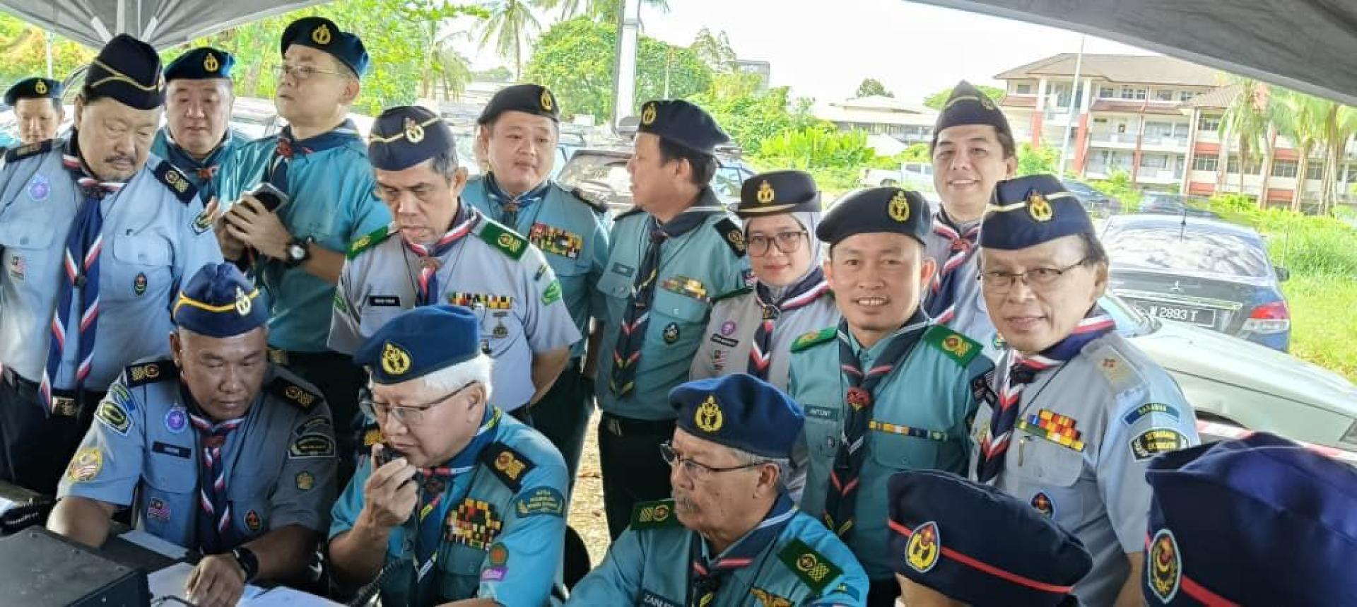 (坐者中间)砂拉越首席童军总监林文明正通过业余无线电与诗巫童军无线电台进行首次连线，现场由多位童军总监及砂童军协会理事共同见证。