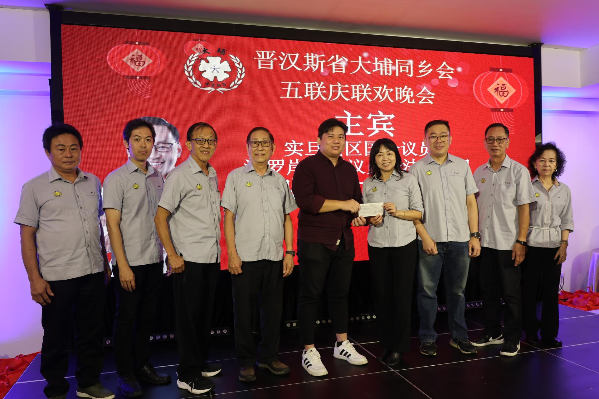 主宾张健仁的代表王恭宇（中）在众理事的陪同下，代为移交拨款支票予主席罗绍凤（右4） 。左起福利主任钟永新、 青年团团长杨咏诒、 秘书丘冠华及署理主席蓝德利；右起为妇女组主任罗秀燕、  财政杨裕腾及筹委会主席谢书暐。