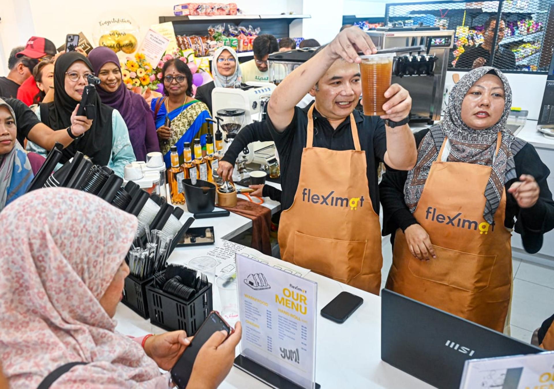 拉菲兹（中）当起超市的“一日店长”，亲自为顾客冲调饮料，引来各族民众捧场。