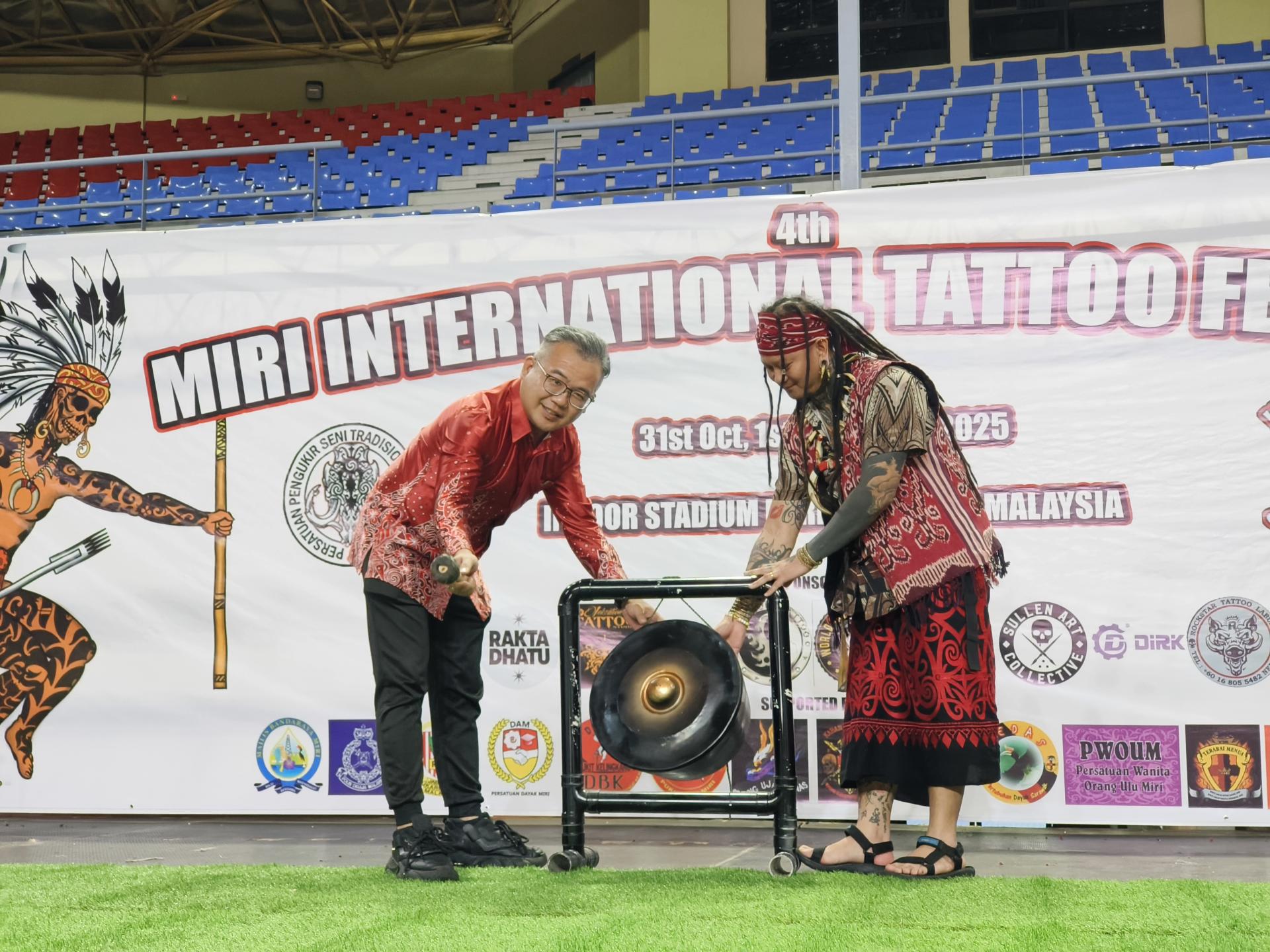 砂交通部长拿督斯里李景胜的代表美里市议员熊千雨为“2025年美里国际刺青嘉年华”主持开幕鸣锣仪式。右为美里肯纳劳传统艺术雕刻者协会主席Sylvester Demeran。