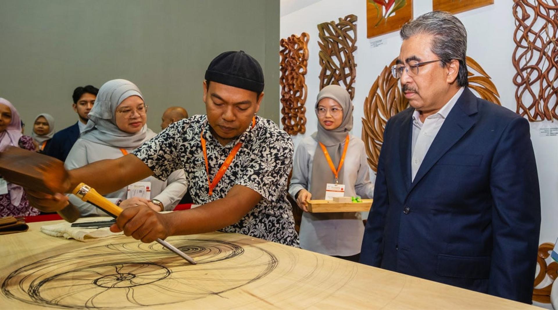 佐哈里（右）参观2025年马来西亚木业博览会展区，并观看木雕示范表演。