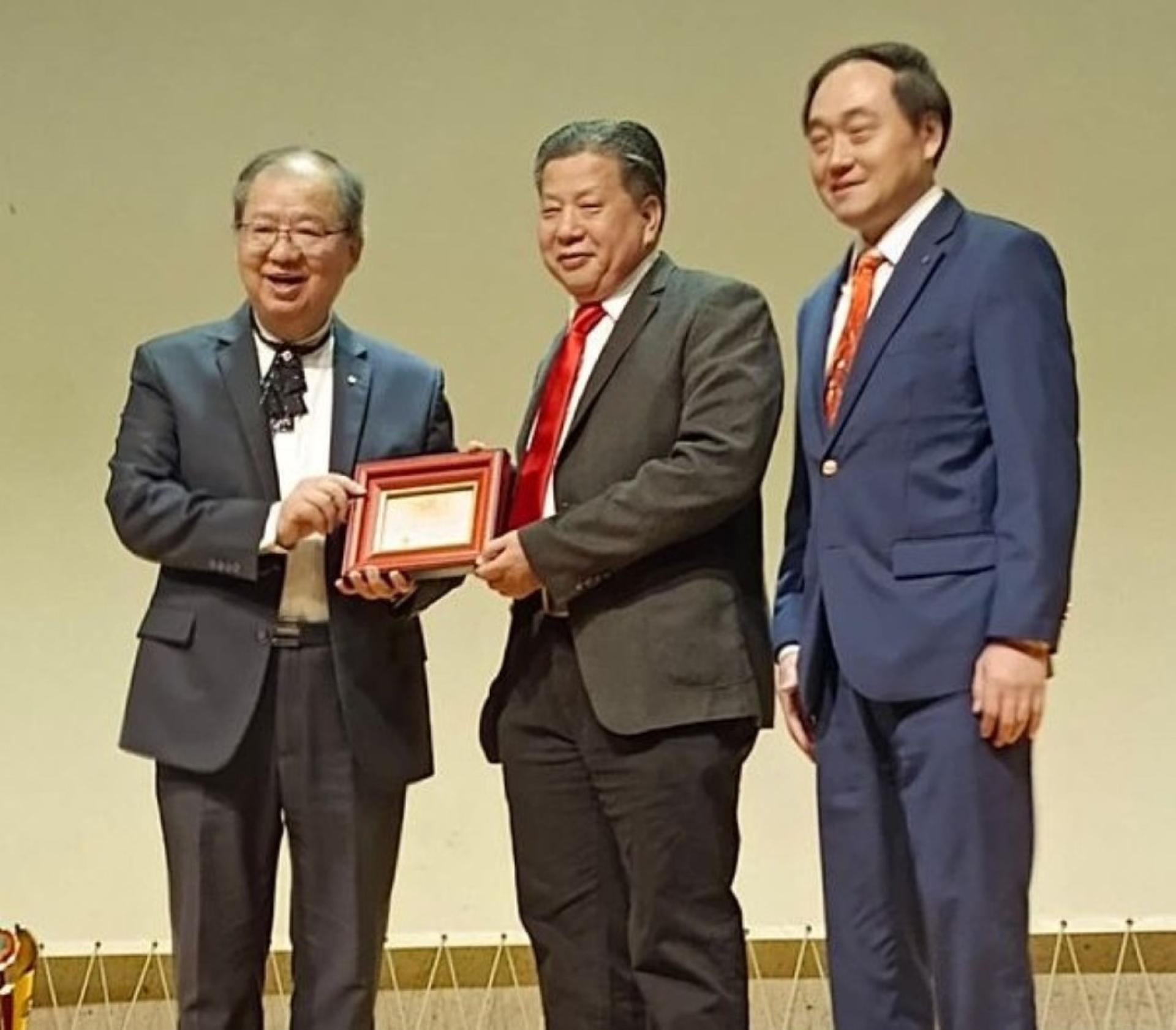砂医总会长江宗兴（中）由世界国际健康管理学会总会长陈秋隆（左）手中接过“十大杰出领导金奖”，右为医学专家载念梓教授。