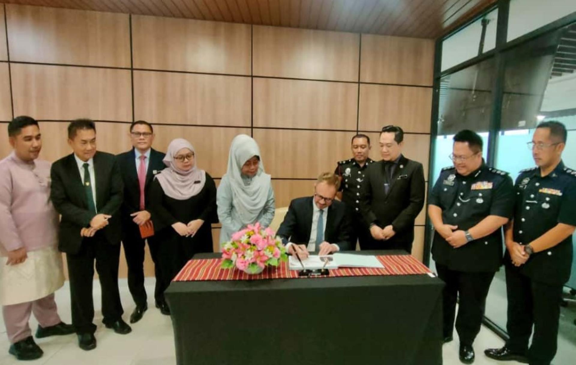 范德文（中坐）在签署访客簿，陈赛明（左5）及其他嘉宾在场见证。