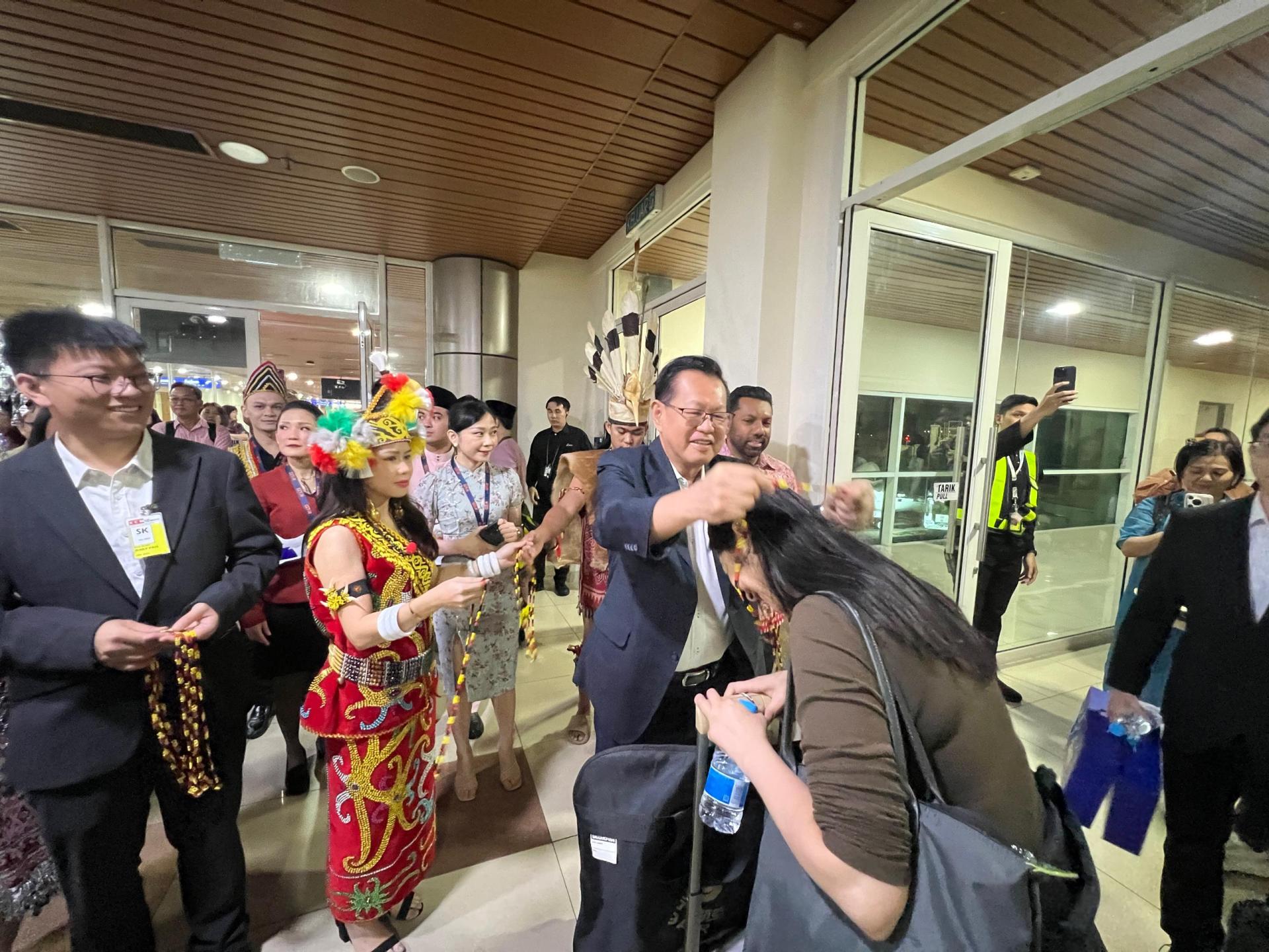 砂拉越交通部长拿督斯里李景胜为抵达乘客挂上砂拉越珠串项链，以示欢迎，左为周朴。