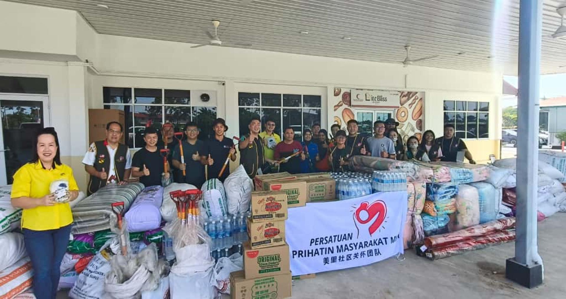 美里社区关怀团队会长李俊达（后排左六）在砂旅游部副部长兼卑尔骚区议员拿督陈超耀代表、其机要秘书谢家洪（后排左七）见证下，移交物资予甘榜威尔乐斯村长鲁斯迪。