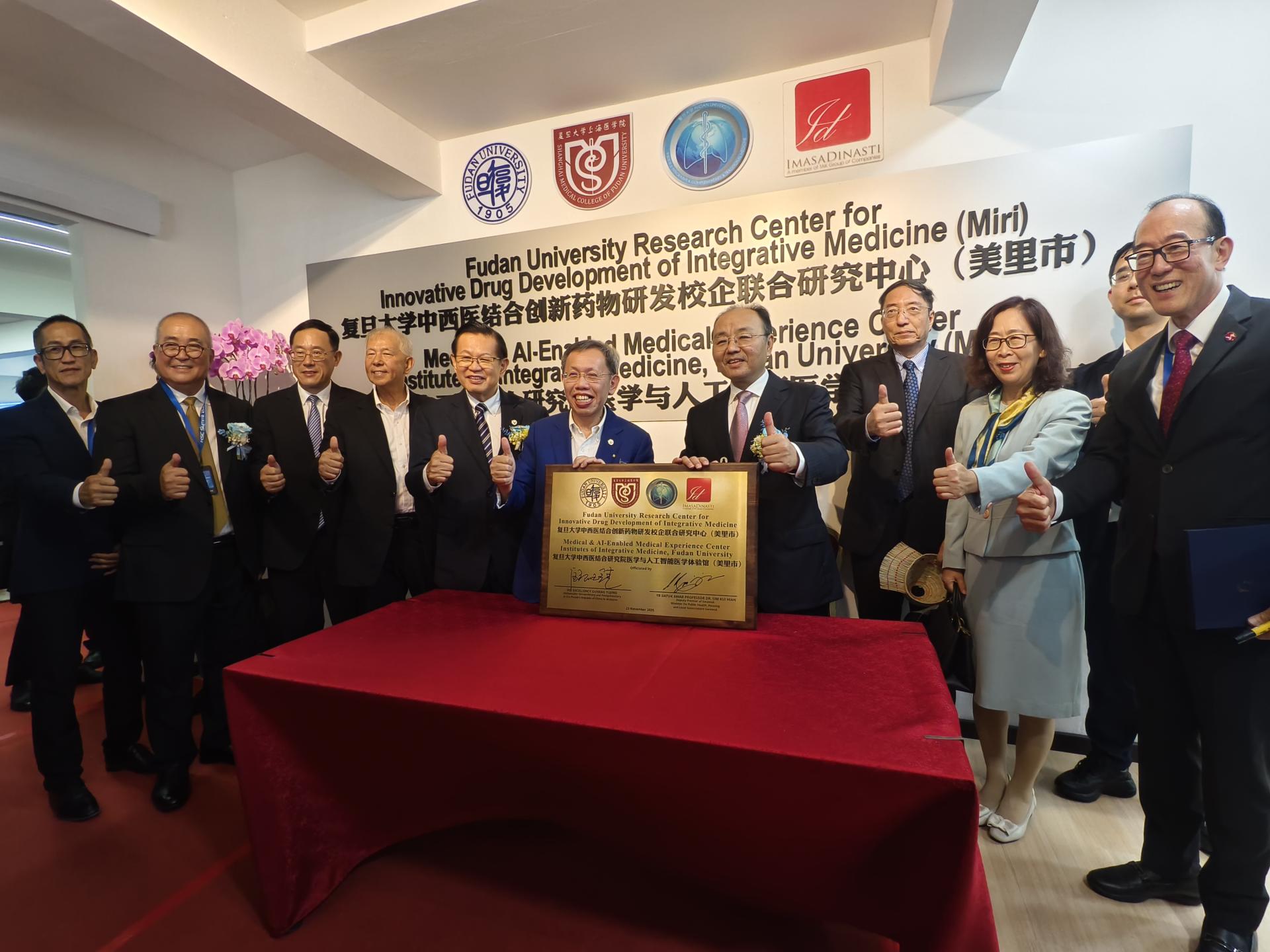 复旦大学中西医结合创新药物研发校企联合研究中心暨人工智能医学体验中心落成嘉宾合影。左2起为美里市长俞小珊、中国驻古晋总领事刑伟平、砂拉越旅游部副部长副部长拿督陈超耀律师、砂拉越交通部长拿督斯里李景胜、砂拉越副总理拿督阿玛沈桂贤医生、中华人民共和国驻马来西亚特命全权大使欧阳玉靖、复旦大学中西医结合研究院院长董竞成、大使夫人宋𣇈梅，以及2025砂邦智慧城峰会筹委会主席兼美砂集团主席张祖德建筑师。