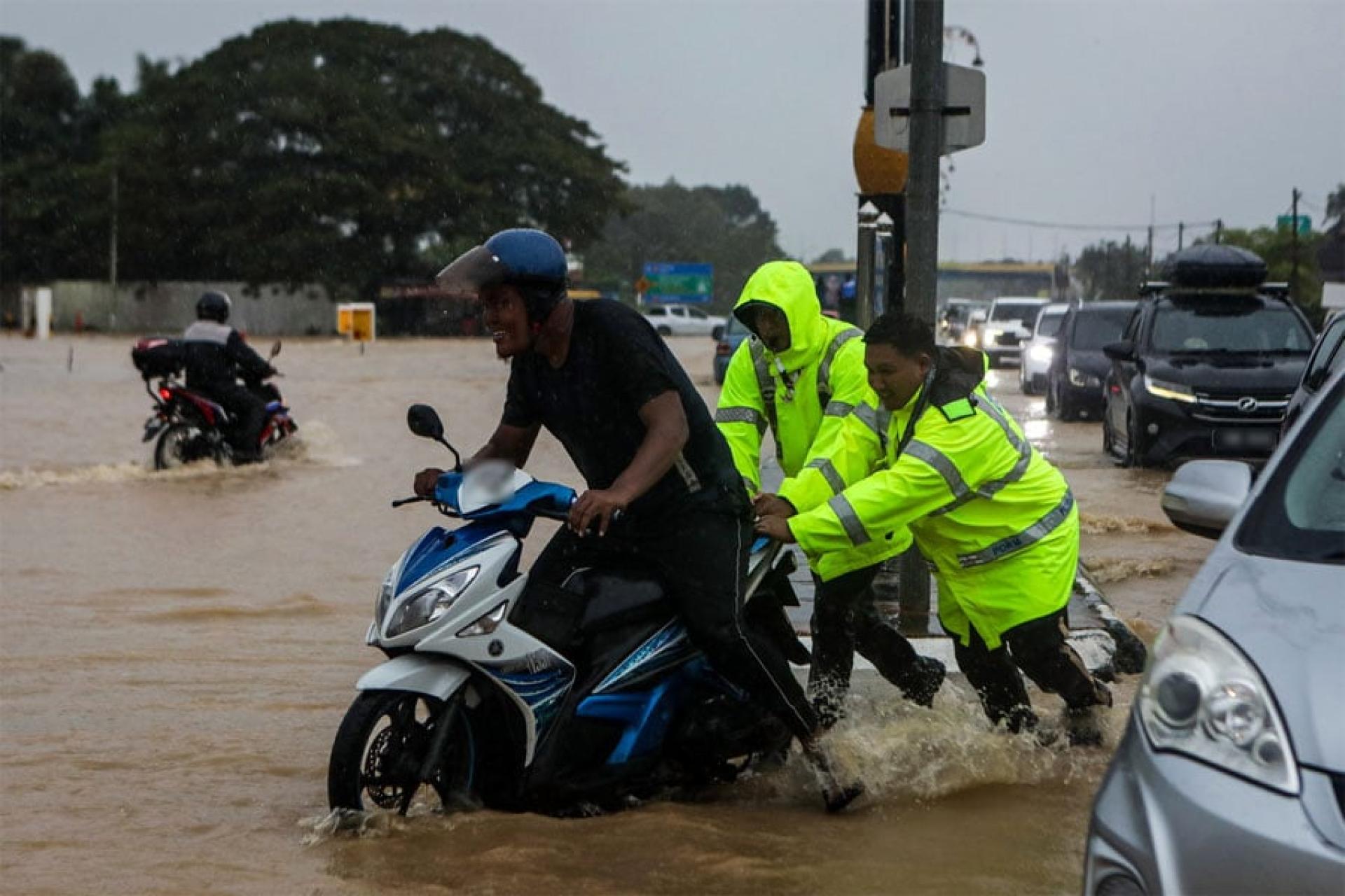 洪水淹没道路，在亚娄指挥交通的交警协助受困的摩托骑士离开淹水路段。