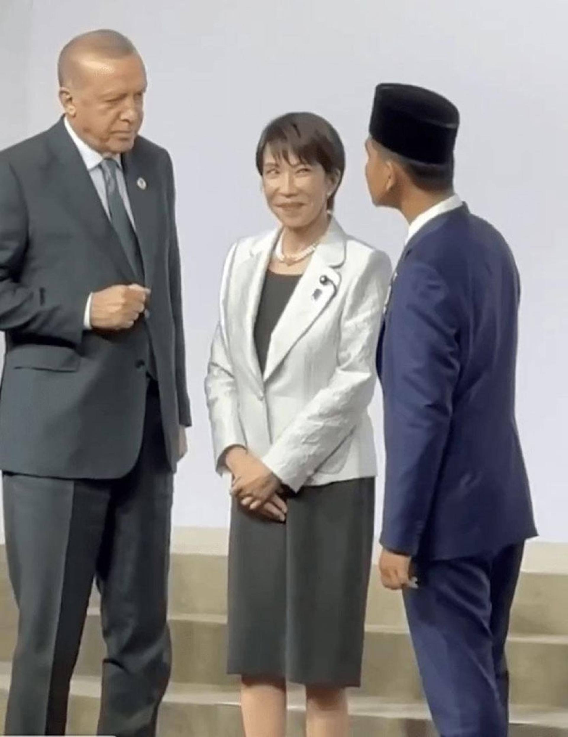 高市站在土耳其总统埃尔多安（左）与印尼副总统拉卡（右）之间，两人正隔着她交谈，身为“夹心位”的高市只能面露尴尬、陪笑硬撑。