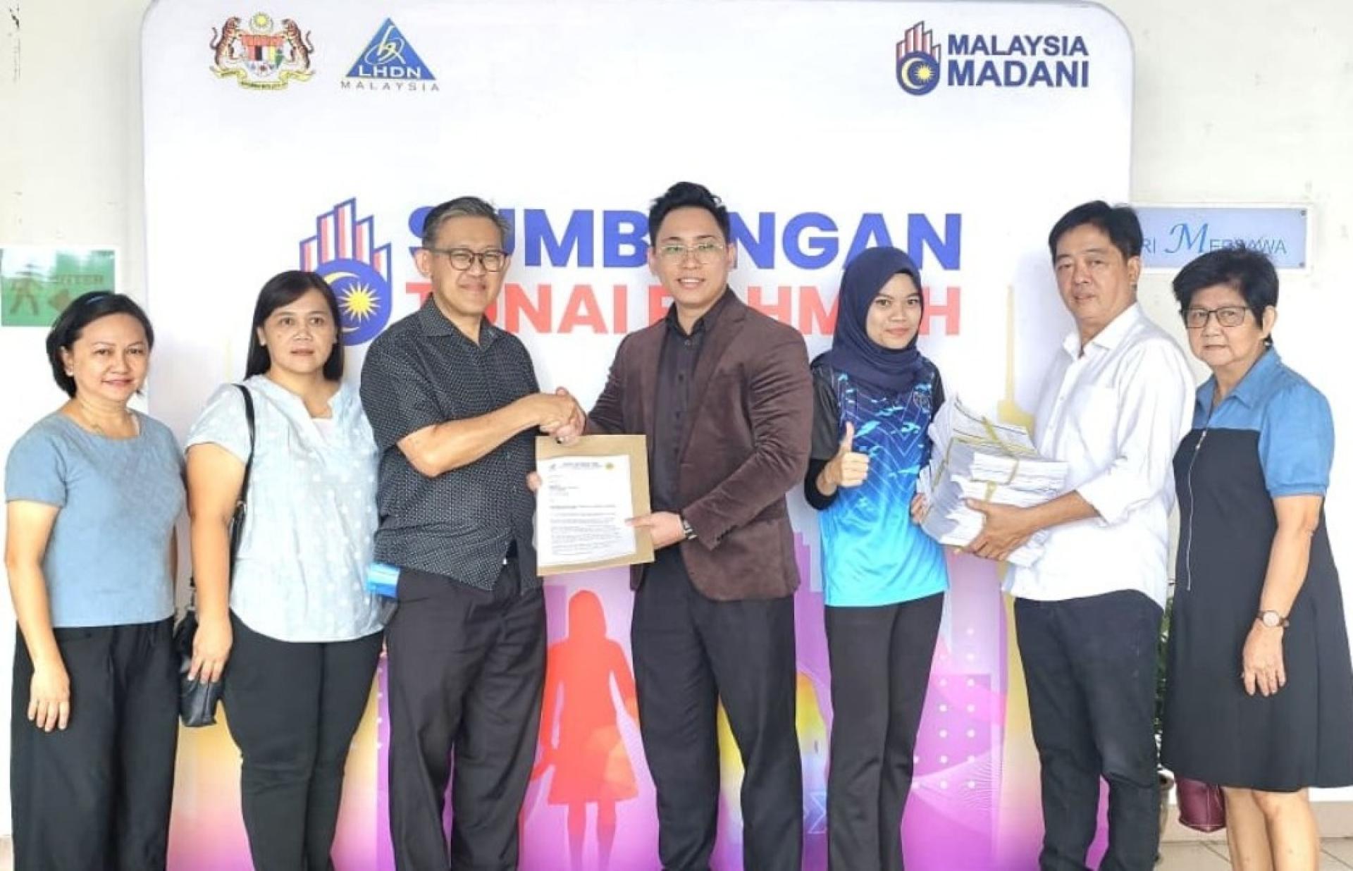 砂人联党峇都林当支部主席薛华东（左3）与副主席许义华（右2）提交为民众填写的STR援助金表格给当局人员。左起为郭小凤、张明妮；右是蔡秋花。