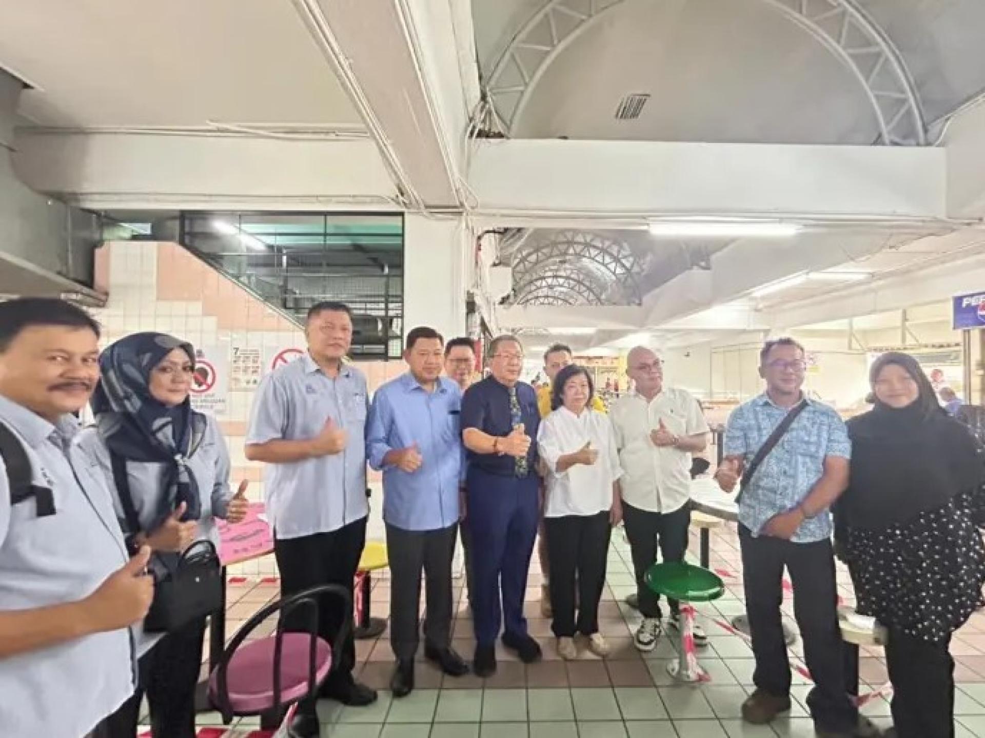 黄鸿圣（左5）与副市长拿督扎耶迪苏海里、议员及市场联络委员会于2025年11月27日在肯雅兰公园市场合影，展示升级后的凳子。