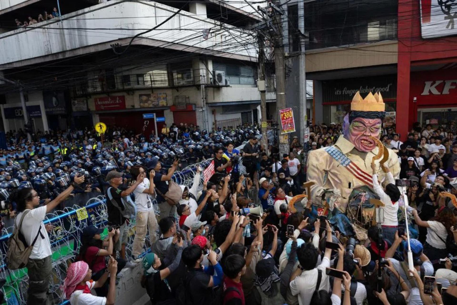 在菲律宾首都马尼拉举行的反腐示威中，示威群众对着总统小马可斯的模拟人像泄愤。大批防暴警察在一旁严阵以待，避免示威现场发生冲突事件。