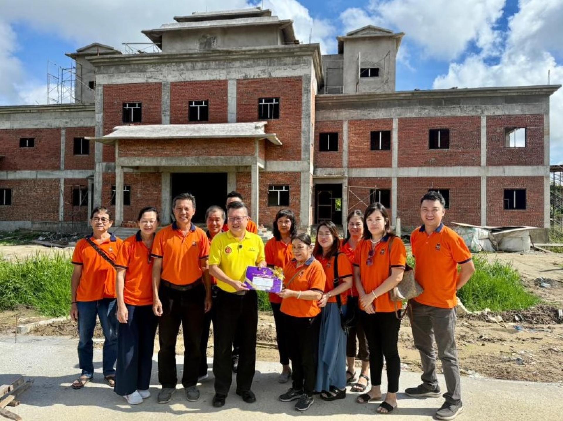 钱进一（左4）在建设工地向梁秋玲移交拨款支票。