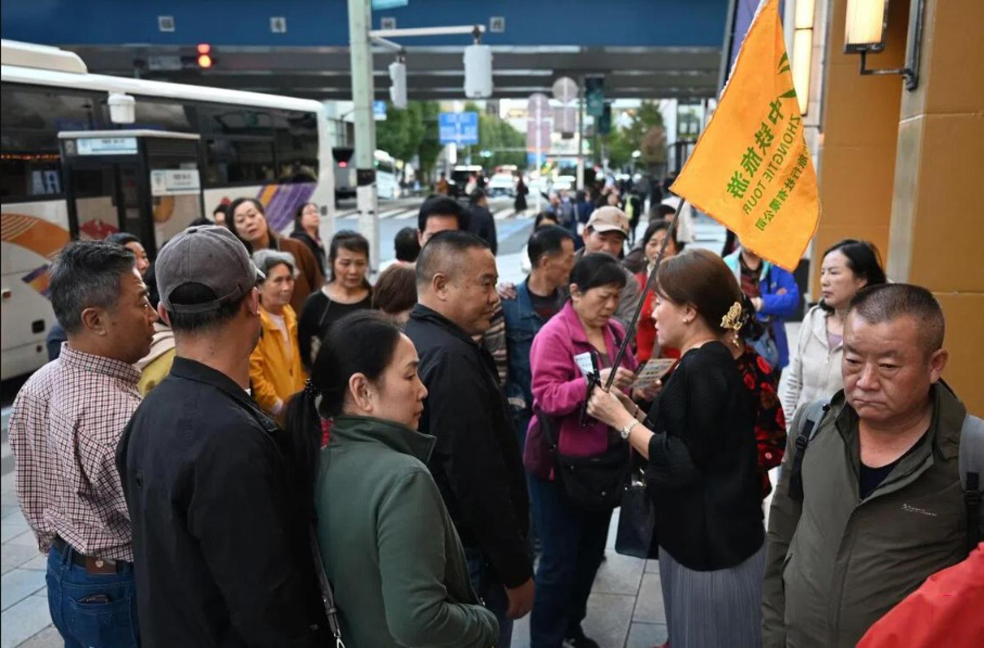 一名中国旅行社的导游11月17日在东京街头向随团的中国游客分发免税店传单。