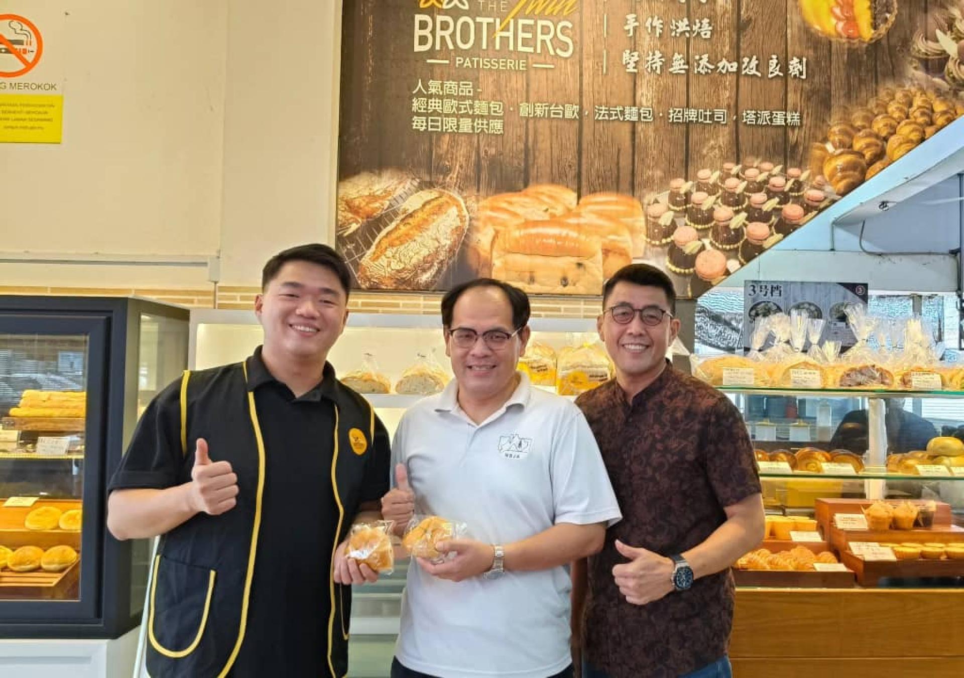 美里双胞胎烘焙坊创办人之一李俊达（左）移交赞助品予北砂新闻从业员协会财政兼筹备会主席杨万勇，右为代代香传饮食坊东主李耘庭。