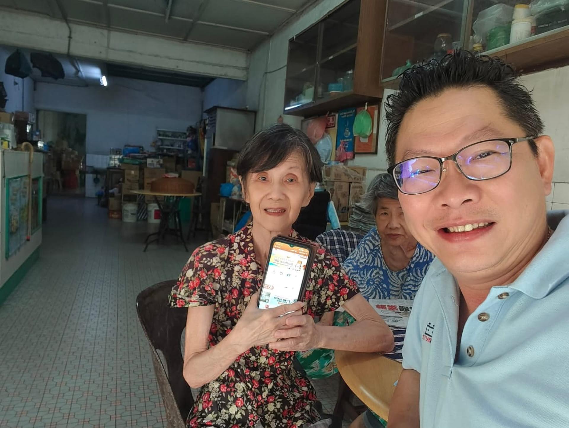 郑志国（右）协助一名长者如何透过电话方式查看援助金。