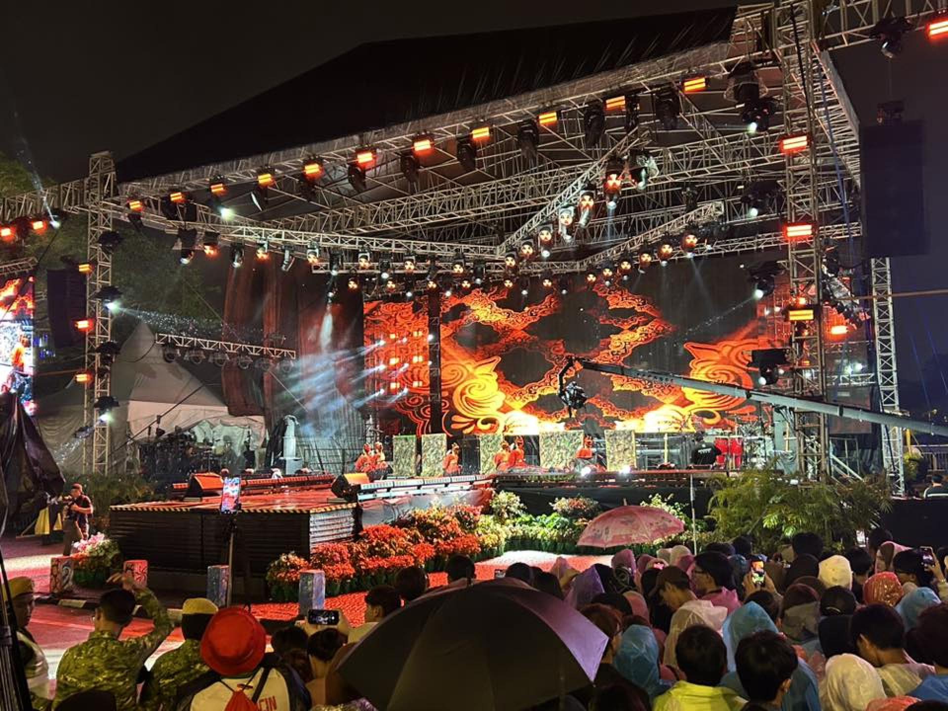 民众撑起雨伞在雨中欣赏艺人们的演出。