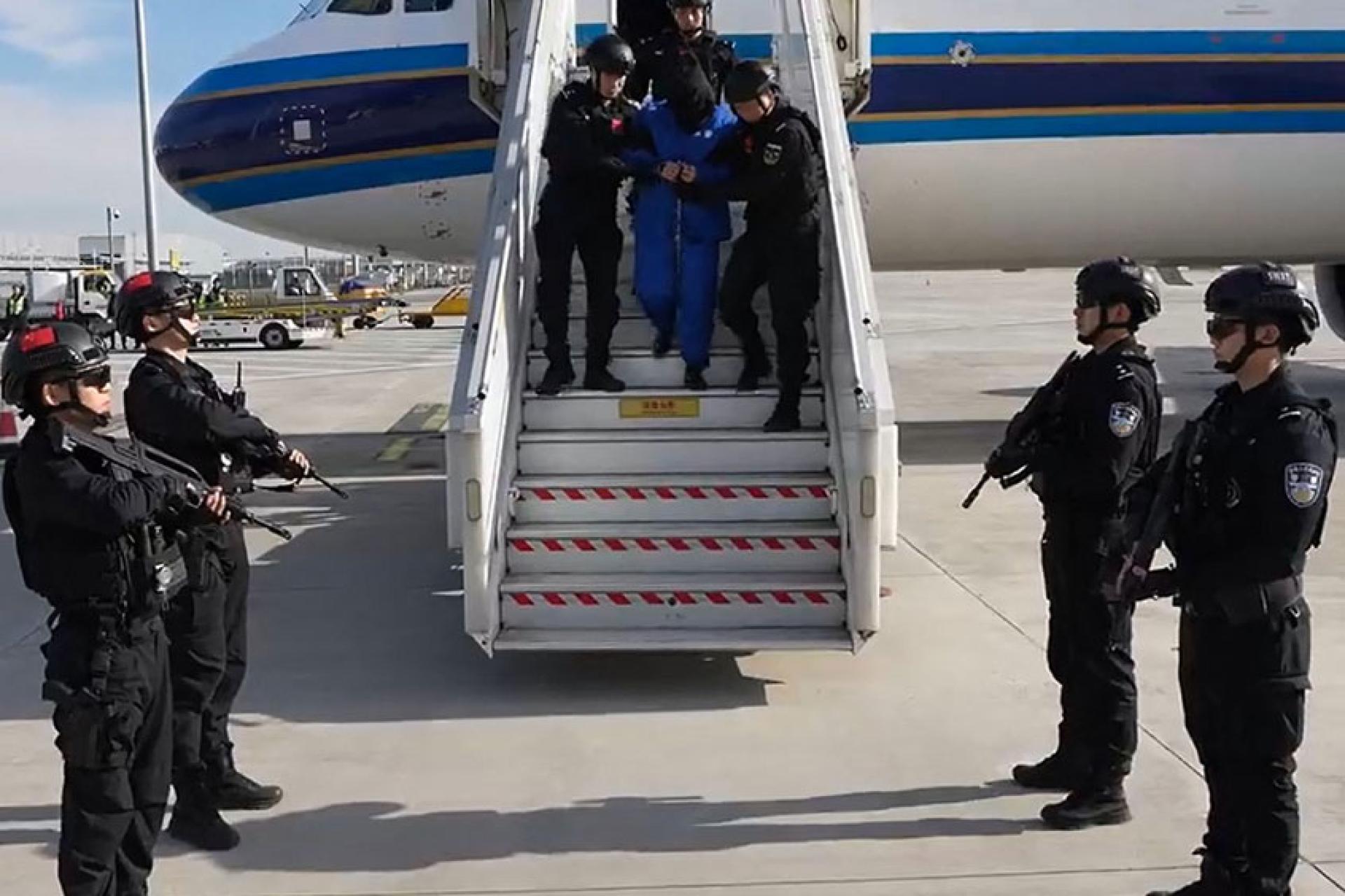 央视公布陈志乘飞机被押返北京的画面。陈志穿蓝色囚衣，戴手铐，多名公安荷枪实弹将他押下飞机。