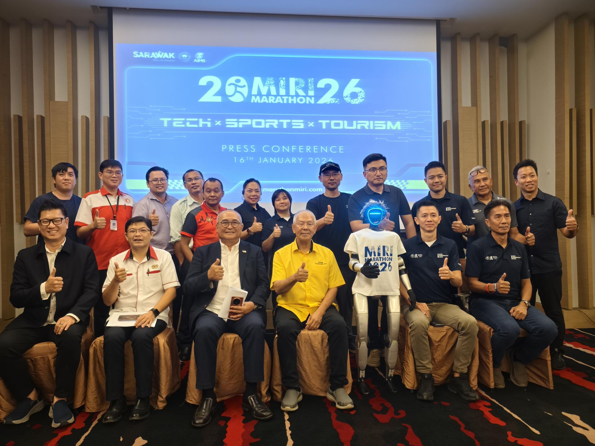 2026年美里马拉松赛筹备会委员在新闻发布会后合影。前排左起为美里市政局旅游发展工作小组主席兼美里市议员范宏祥、美里医院院长黄修儒医生、美里市长俞小珊、砂旅游部副部长兼卑尔骚区州议员拿督陈超耀、命名为“美里”人形机器人、杨惠德，以及邓瑞民。