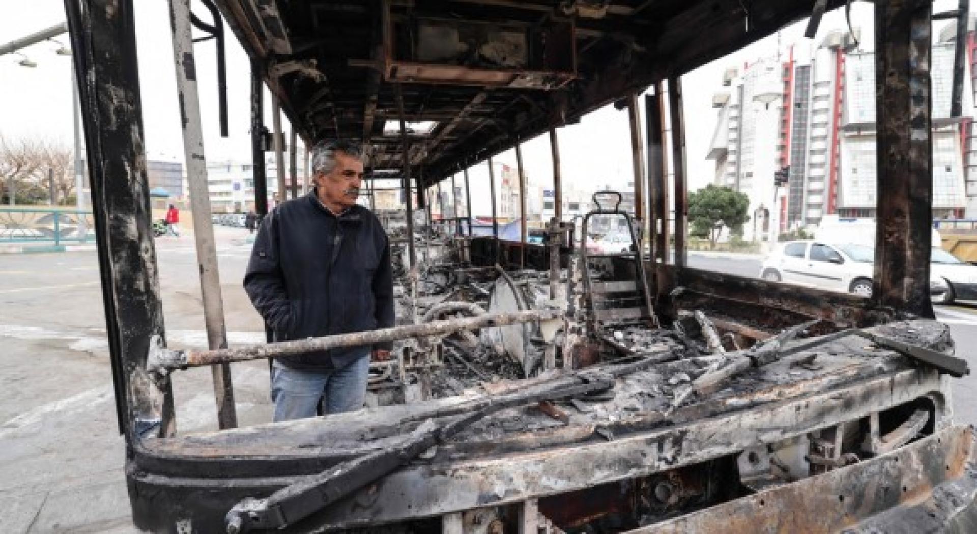 在德黑兰萨德吉耶广场，一名男子站在被烧毁的公交车残骸旁。
