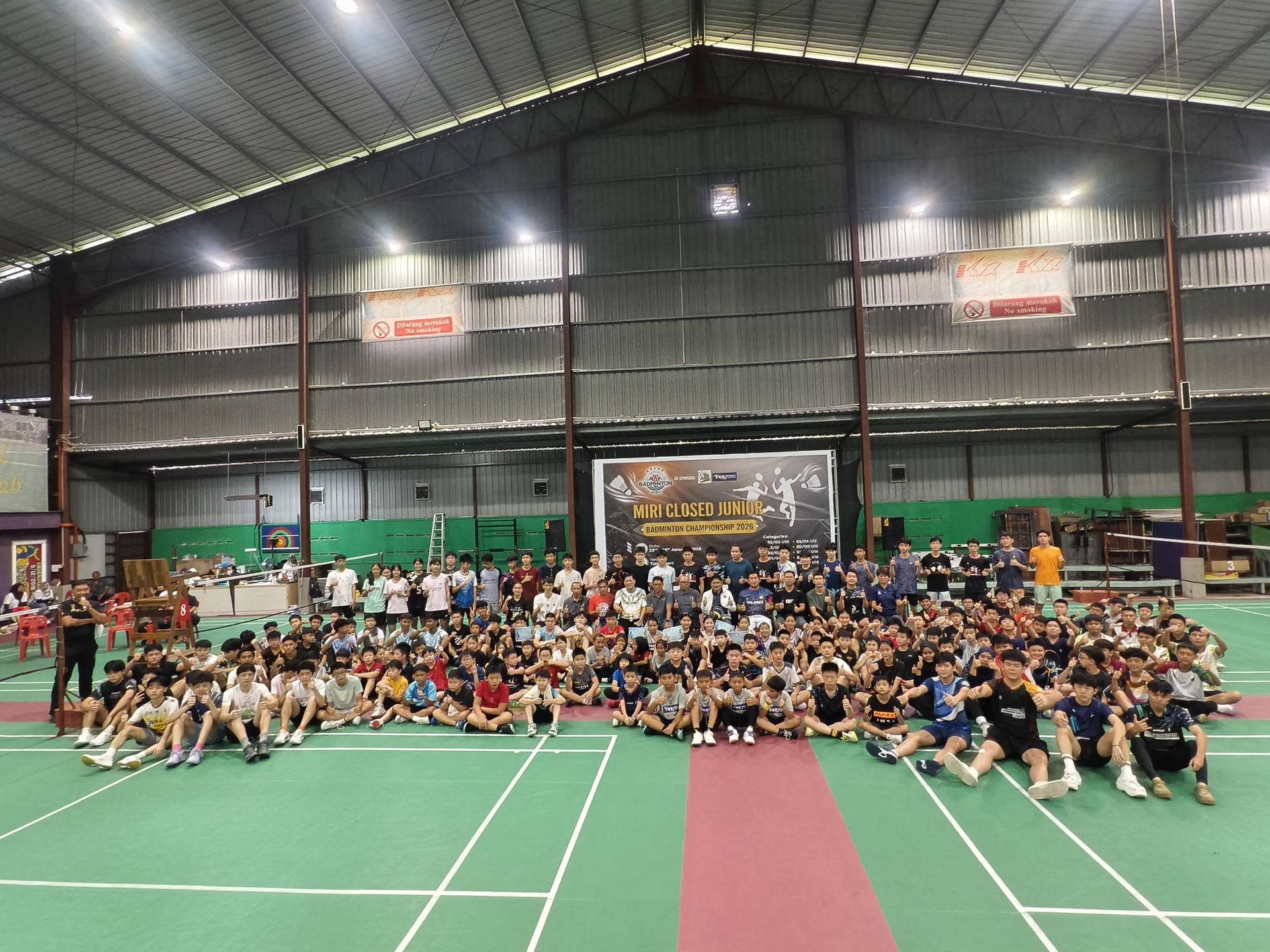 主办单位、赞助商、嘉宾、教练及全体参赛球员在2026年美里青少年羽毛球锦标赛闭幕式后大合影，场面热闹，展现美里羽球基层发展的蓬勃气象。