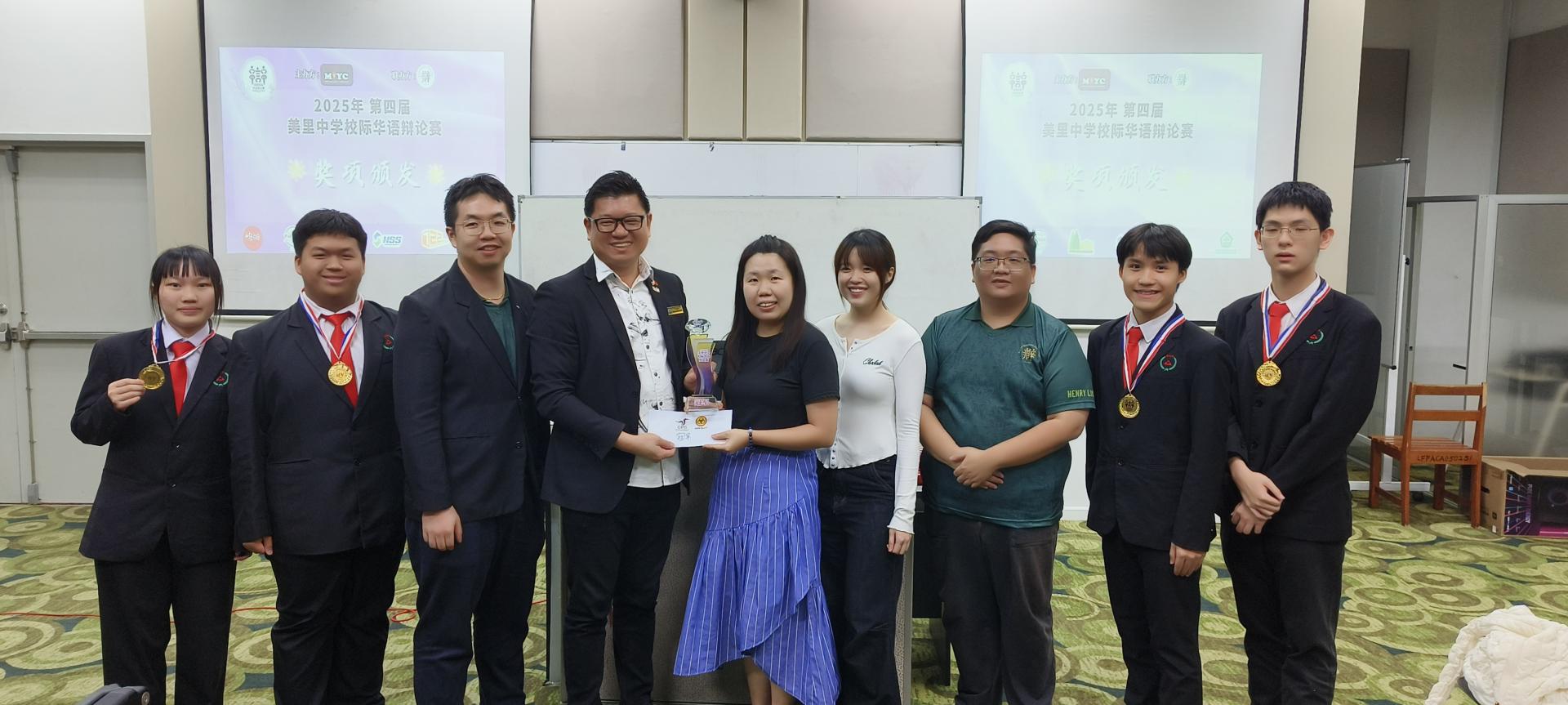 美里校际华语辩论赛中，培民中学A队夺冠。培中林镁晶老师（右5）、许慧盈教练（右4）从砂拉越人联党埔奕支部组织秘书兼美里市议员范宏祥（左4）手中接过奖杯。