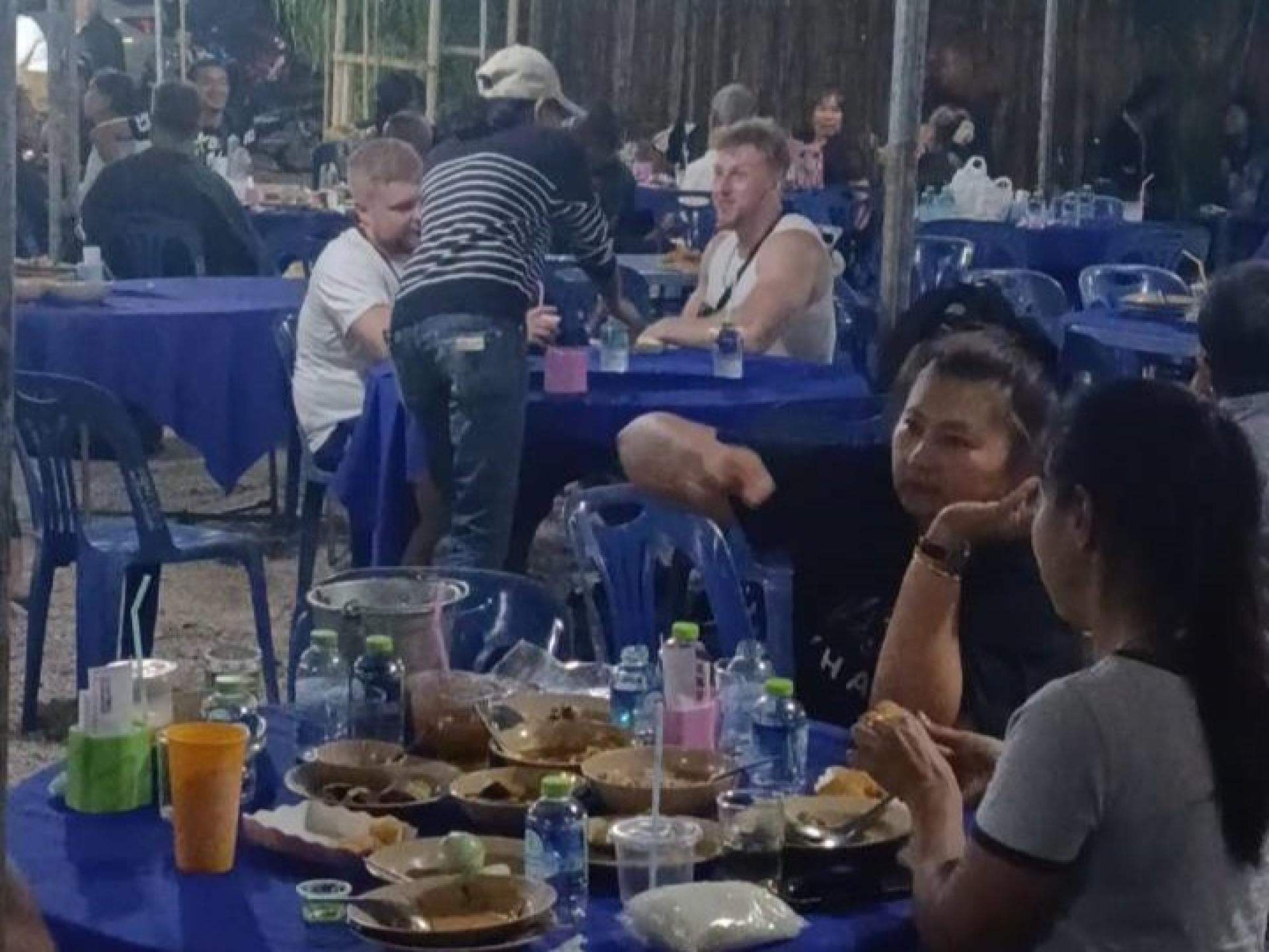 几名外国游客走到摆放着各式餐点的长桌前，以为这里是夜市摊位，没想到不仅没有被丧家请离，反而被热情款待。（图片来自Charantorn Chareomkiad）