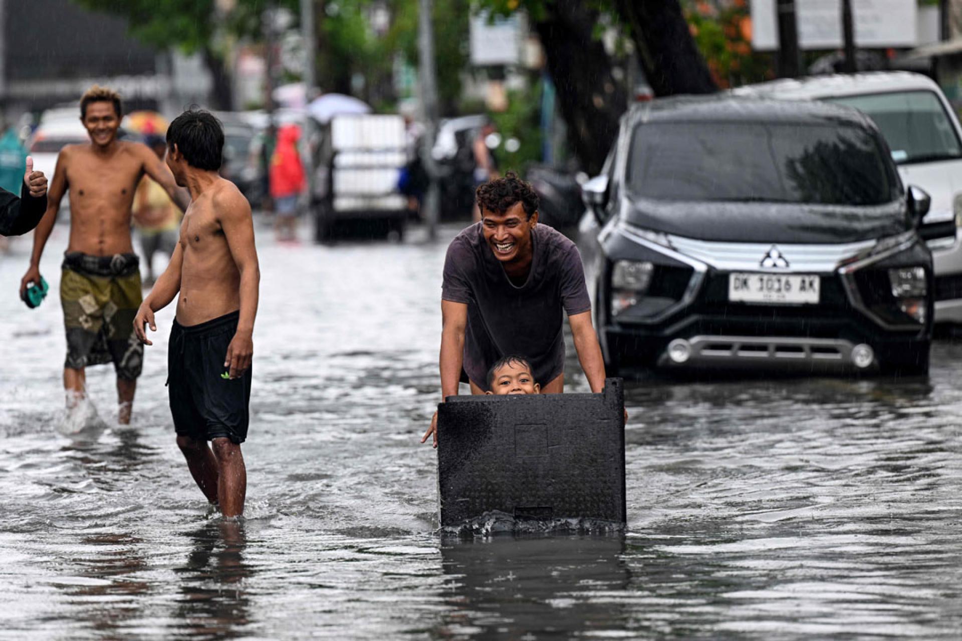 巴厘岛遭遇暴雨袭击后，一名男子24日推着坐在容器里的孩子穿过被洪水淹没的街道。