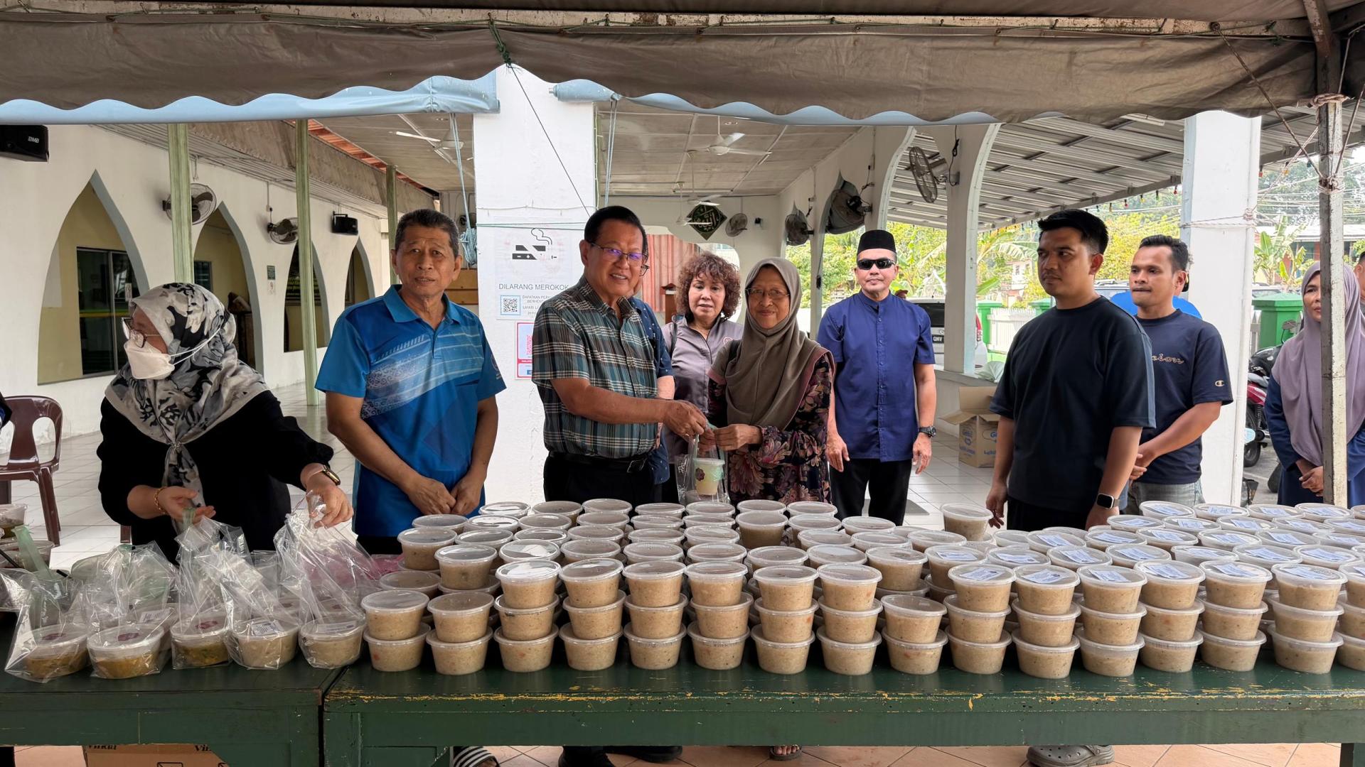 李景胜（左）出席甘榜埔奕丹绒巴都施赠杂锦粥活动，分派杂锦粥予当地居民。