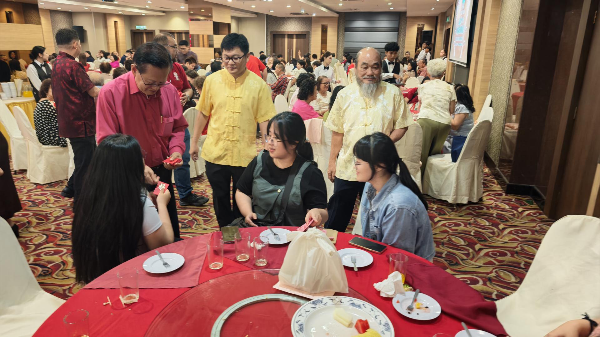 拿督斯里李景胜（左2）在筹备会主席蔡明勇的陪同下，派发新年红包予出席晚宴宗亲。