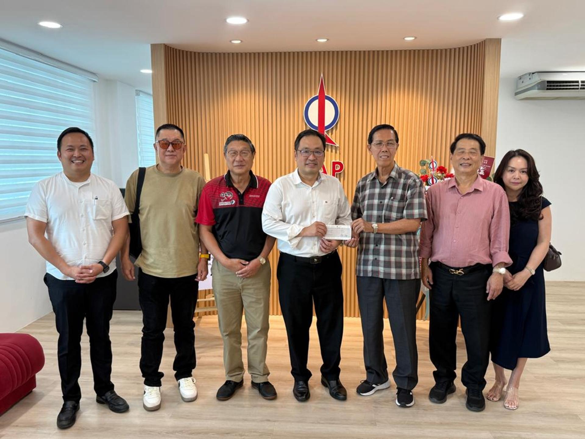 张健仁（中）在众人的陪同下，移交拨款支票予主席周政光（右3）。左起为张健仁特别助理江峰年、乒乓主任/教练陈振武、副主席陈世金；右起为会长何长舜伉俪。