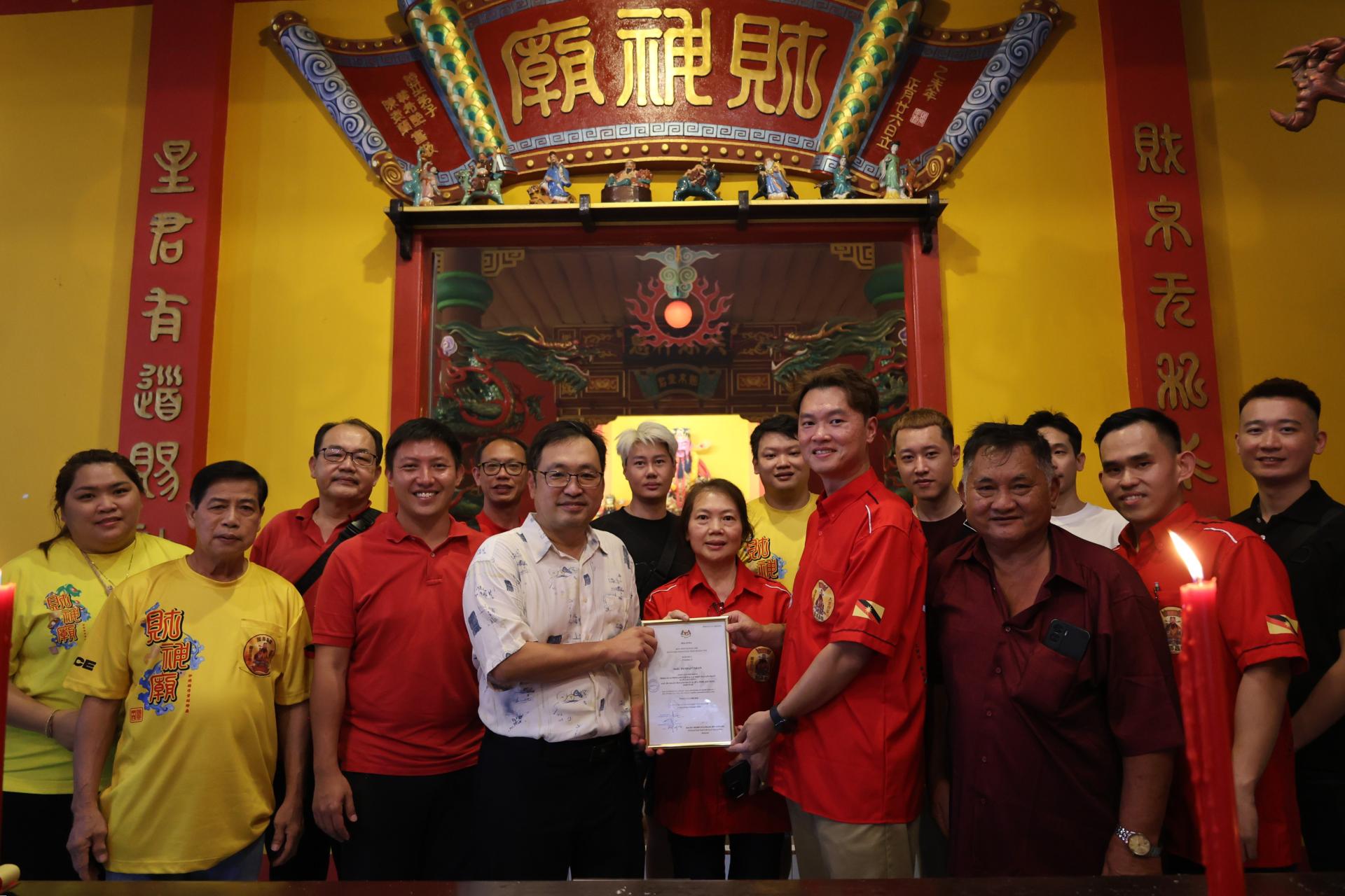 张健仁（左5）在特别助理沈杰龙（左4）及一众财神庙理事及众人的陪同下，移交社团注册局的证书予主席罗俊龙（右4）。