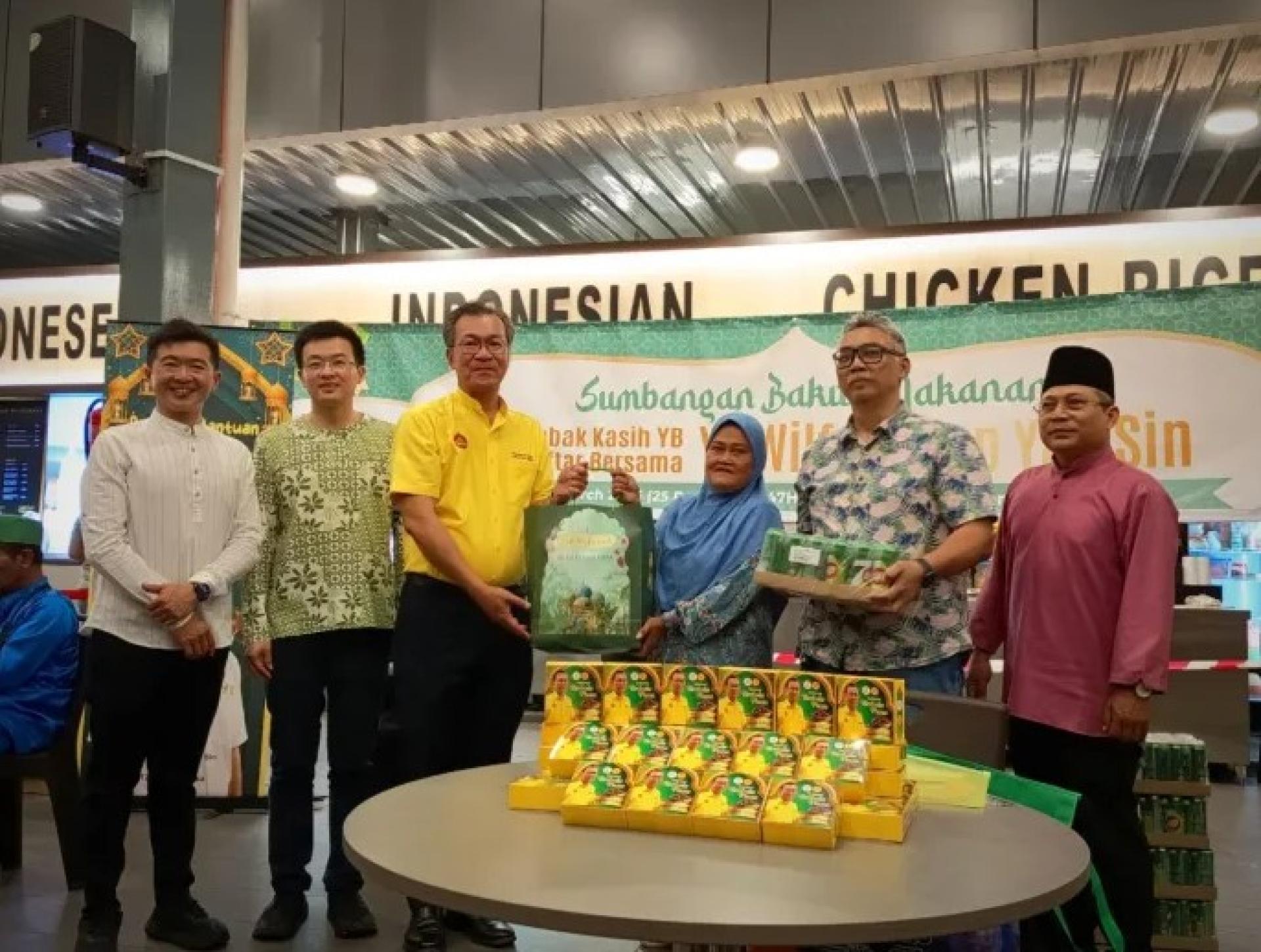 叶耀星（左3）在3月15日Farley Mall的“YB爱心食篮”派发计划中向一名受助者递送食物篮，其他人围观。