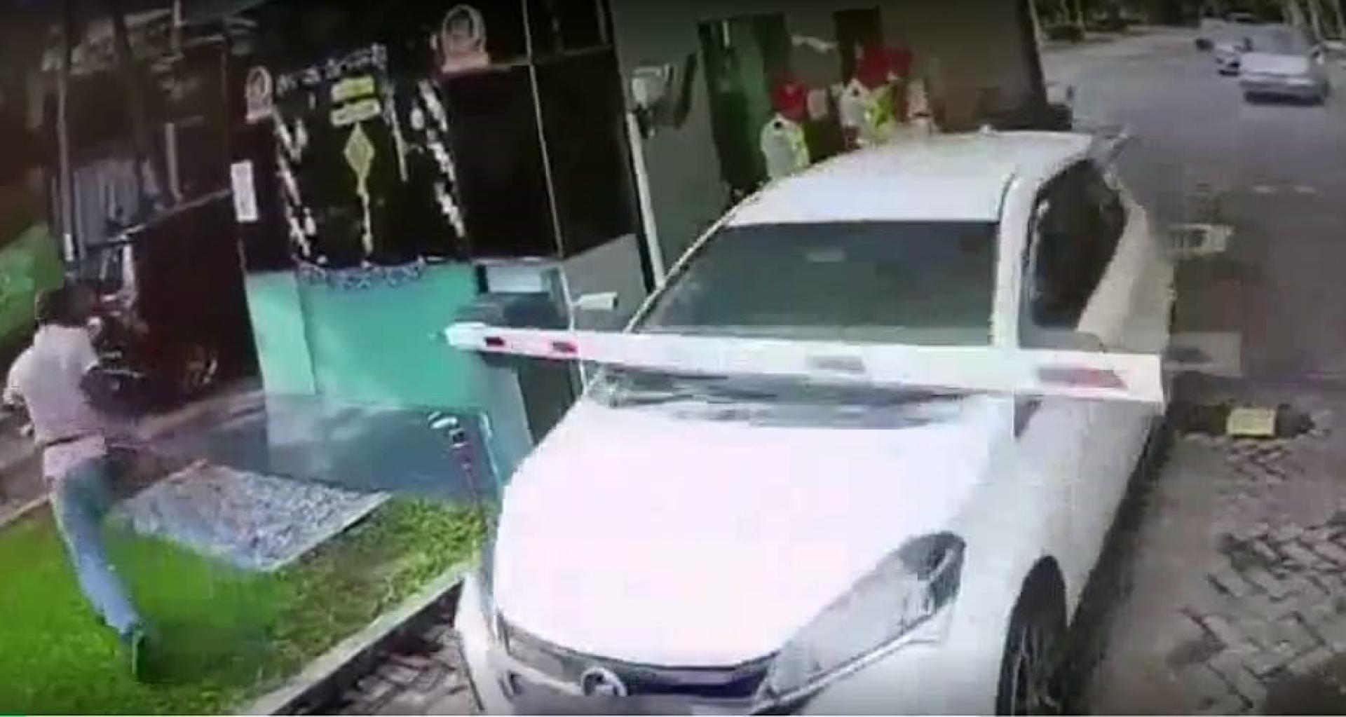 轿车撞破电动栏杆后离开，围观男子及时躲避。