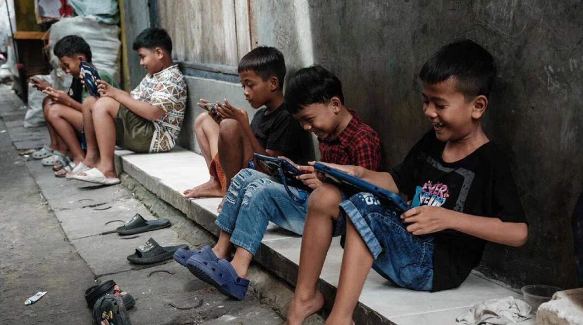 雅加达一群小男孩聚在街边，用手机和平板电脑打游戏。