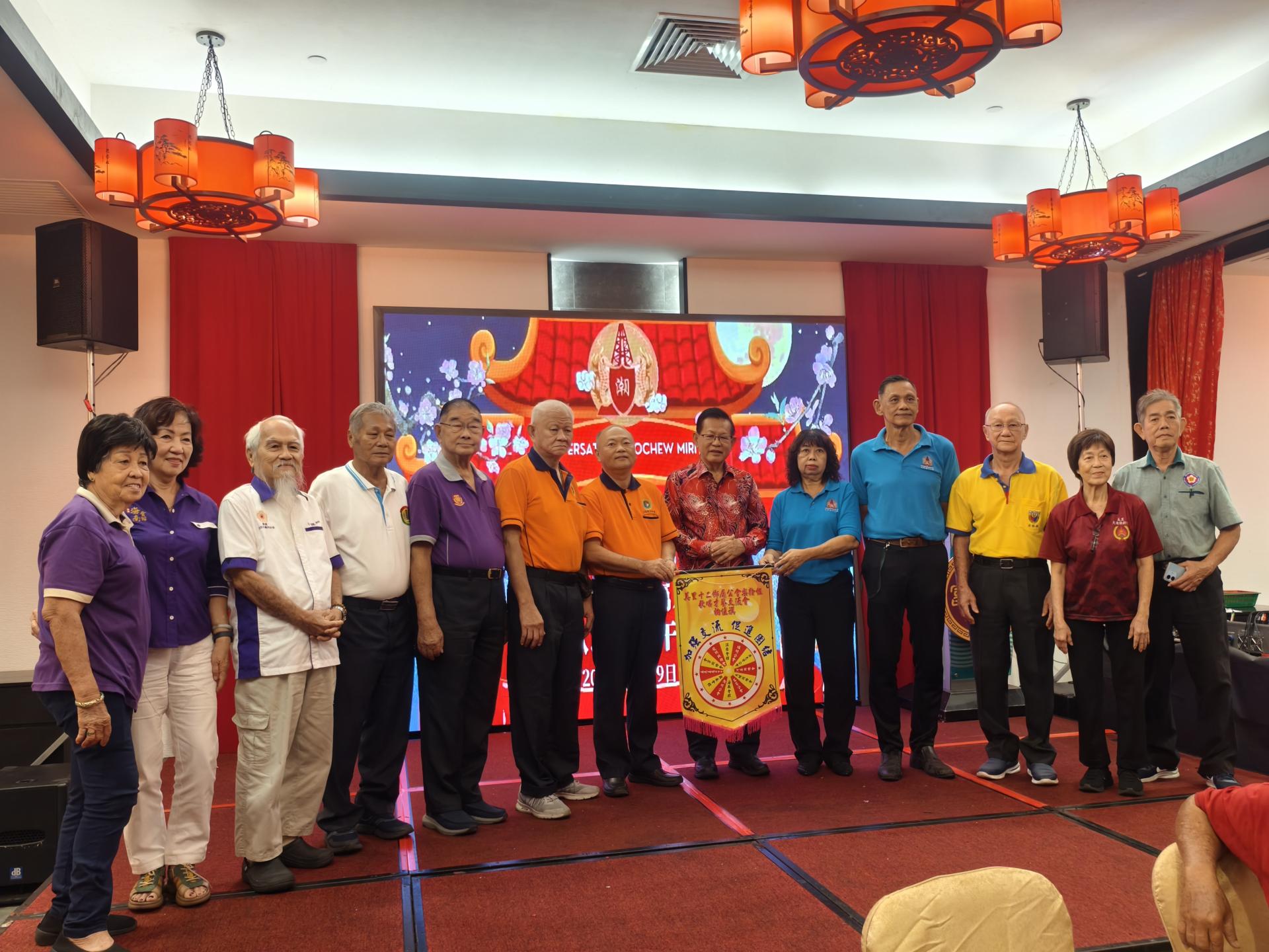 美里潮州公会乐龄组主任杨銮娇（右5）在砂交通部长兼永久名誉顾问拿督斯里李景胜见证，各乡属公会乐龄组主任陪同，移交轮值主办锦旗予美里兴安会馆乐龄组主任陈国荣（左7）合影留念。
