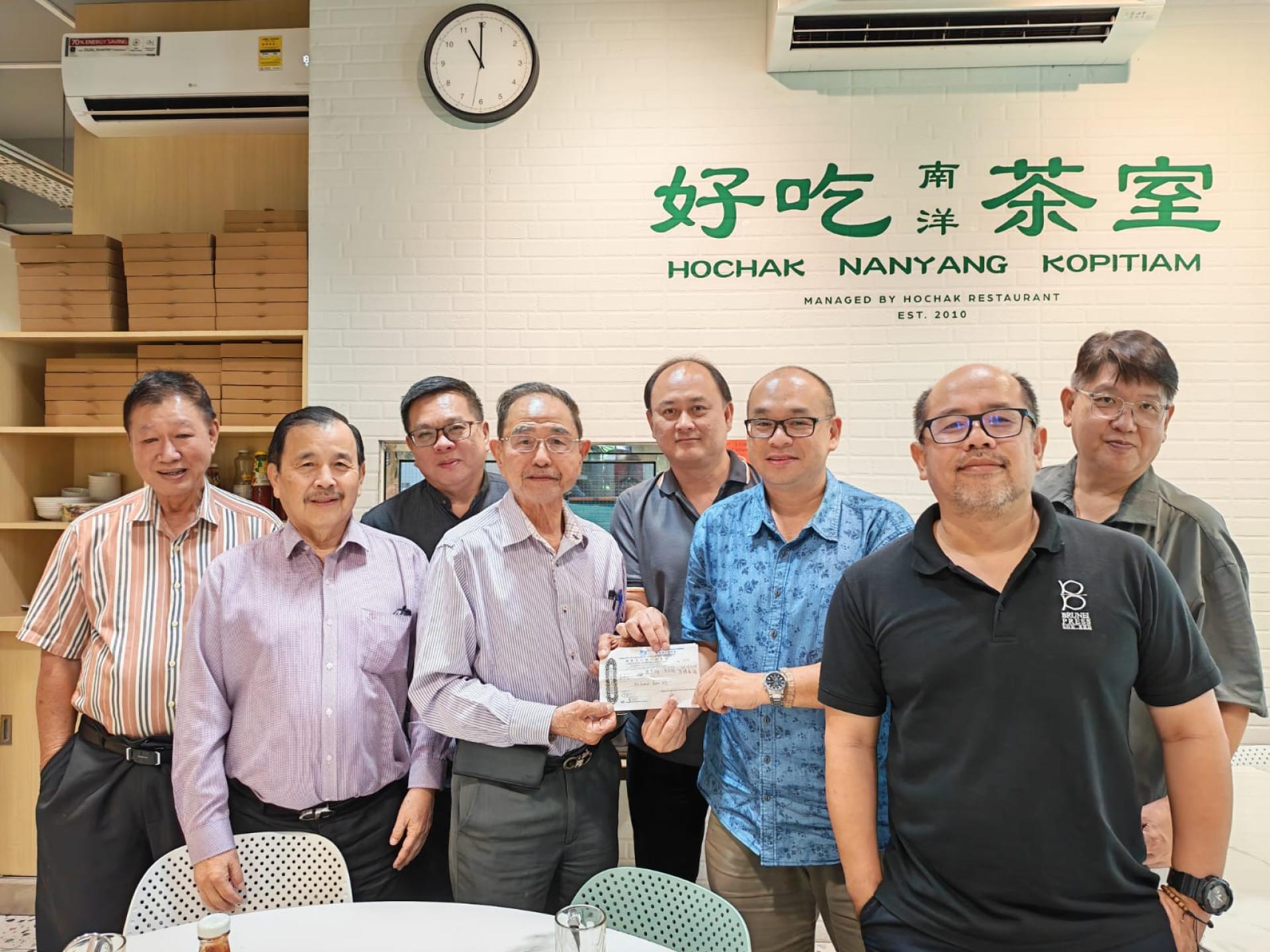 右三起为汶莱媒体记者记者朱芑雄与记者方文杰一起代表移交款项，由汶莱华人慈善会会长孙胜利代表接领。左二为该会理事林登财与各报媒体记者合影。