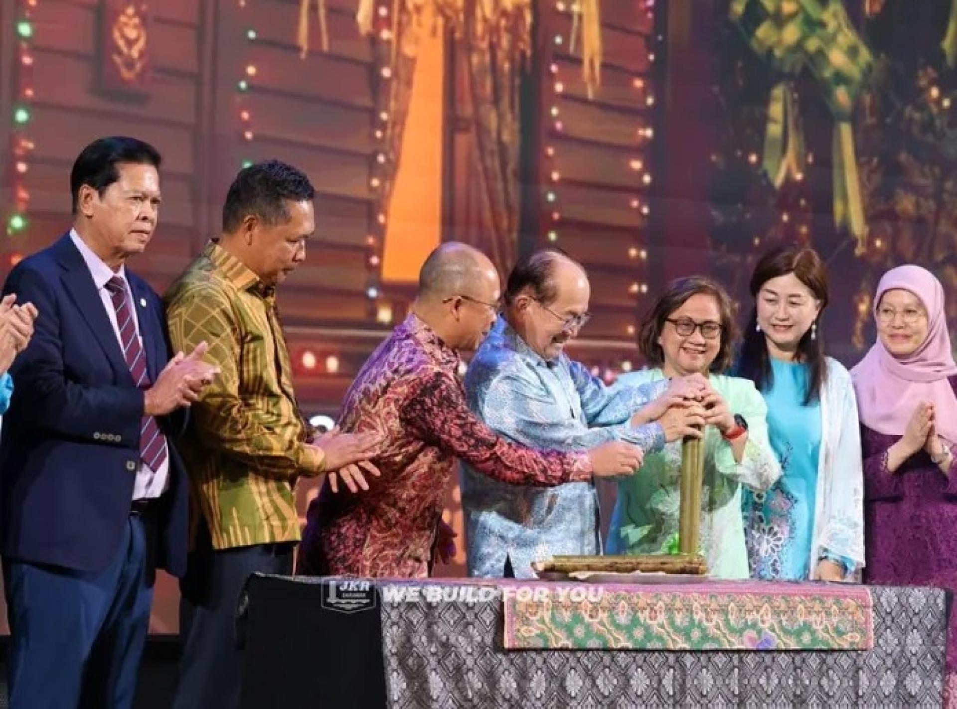 道格拉斯（右3）与夫人多琳（右2）在4月6日其他宗教事务单位综合大厦的公共工程局砂拉越开斋聚会上分食竹筒饭，旁观的有局长Cassidy（左3）及其他贵宾。照片来源：砂公共工程局。