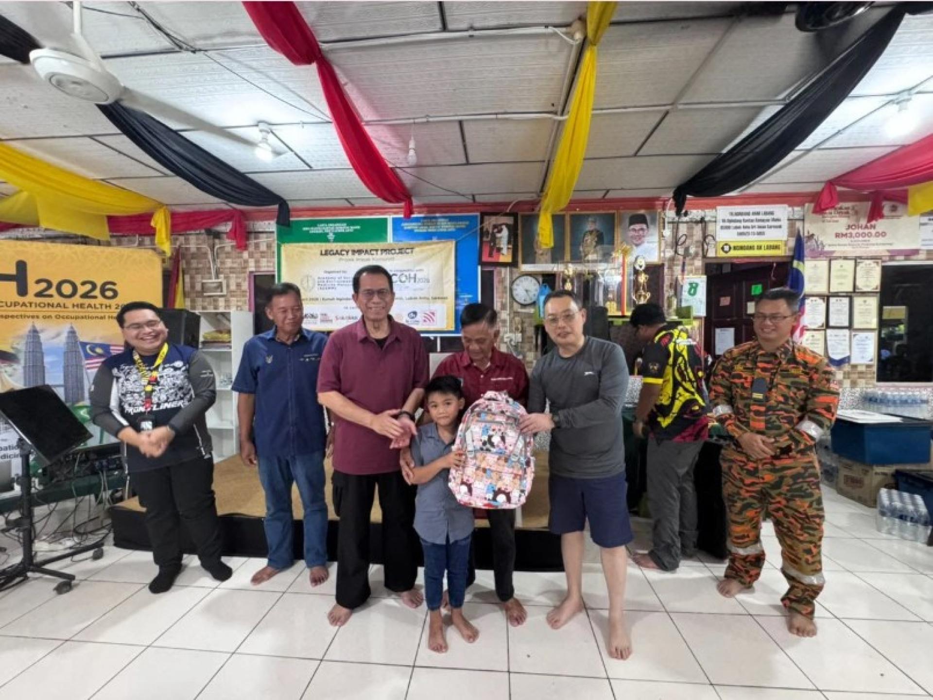 阿布哈桑博士（左3）在ACOH 2026农村推广项目中向Rumah Ngindang的一名年轻居民赠送礼物。