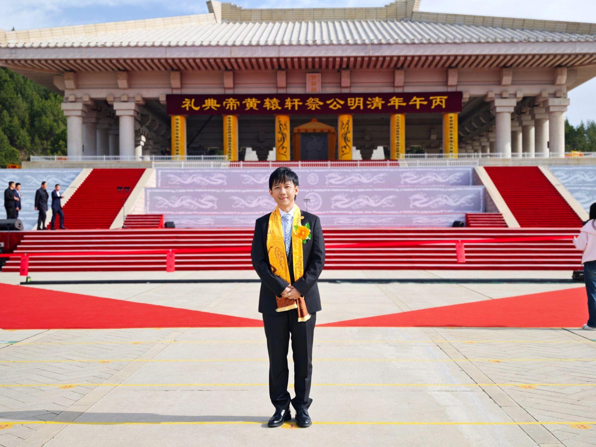 阿牛应邀出席公祭轩辕黄帝典礼，佩戴黄色佩巾，肃立于气势恢宏的轩辕殿前。