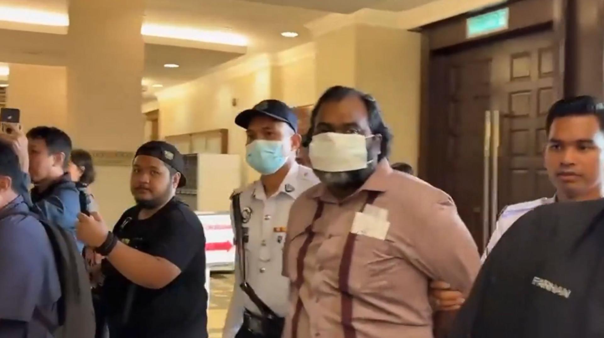 疑犯被带到吉隆坡法庭面控，他戴著口罩，在交警的拘押下抵达法庭。（马新社视频截图）