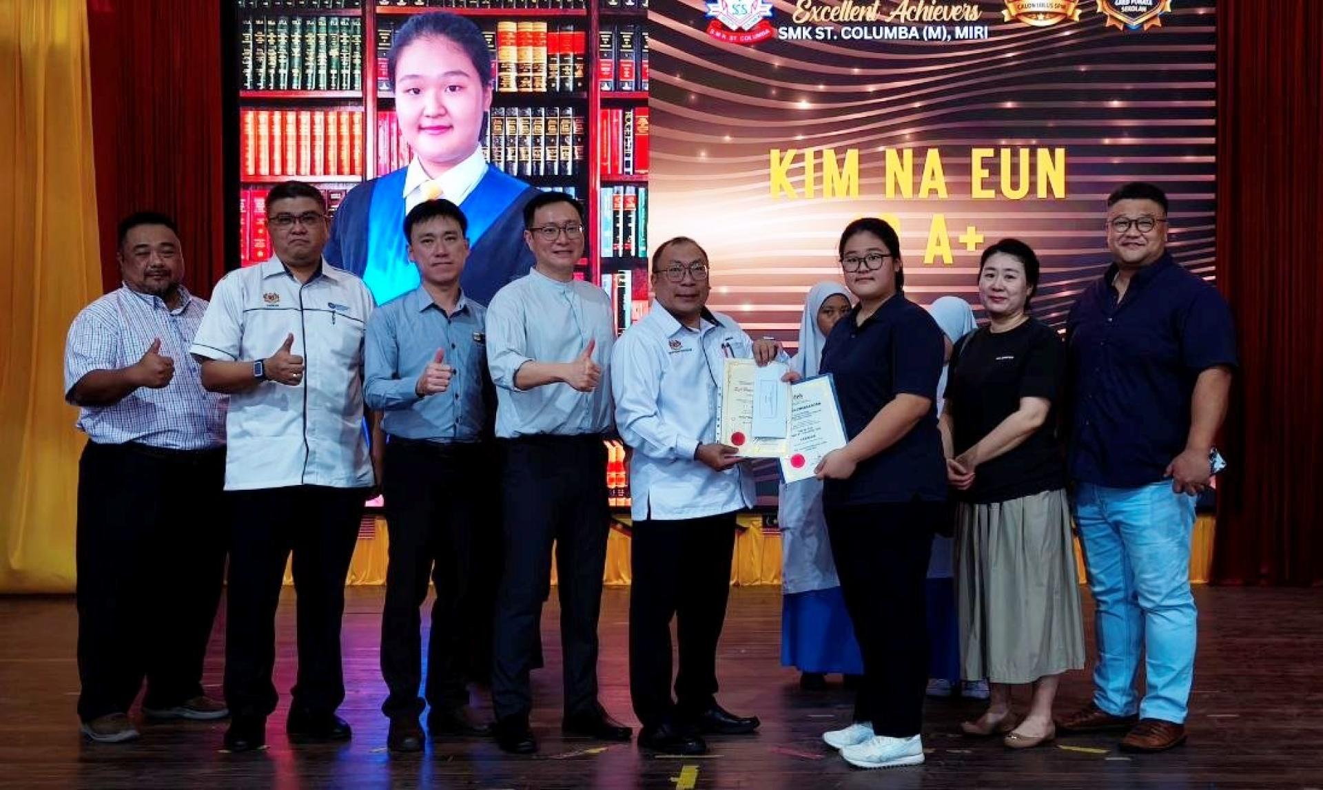 圣哥伦巴中学校长金本马桑（左5）颁发优秀证书与奖励金予金娜恩（右3），其在SPM报考10科  皆考获A+；右1及右2为其家长。左4为家协主席陈永明，左3为行政副校长黄孝铭，左2为学生事务副校长林颂  强，左1为课外活动副校长保罗亨利。
