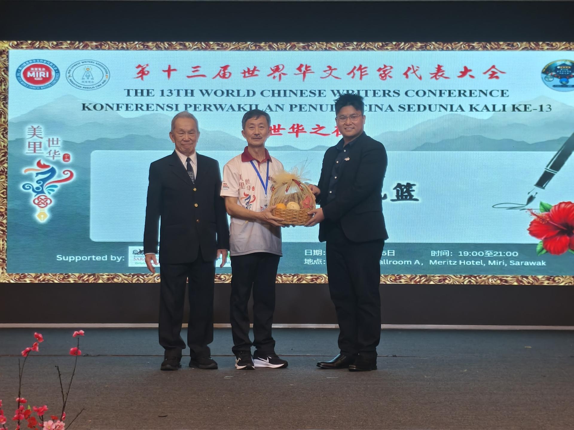 美里笔会主席兼第13届世界华文作家代表大会筹备会主席许敬平赠送纪念品予“世华之夜”主宾赵俊文，由代表邹梓建（左2）接领。左为大会主席孙德安。