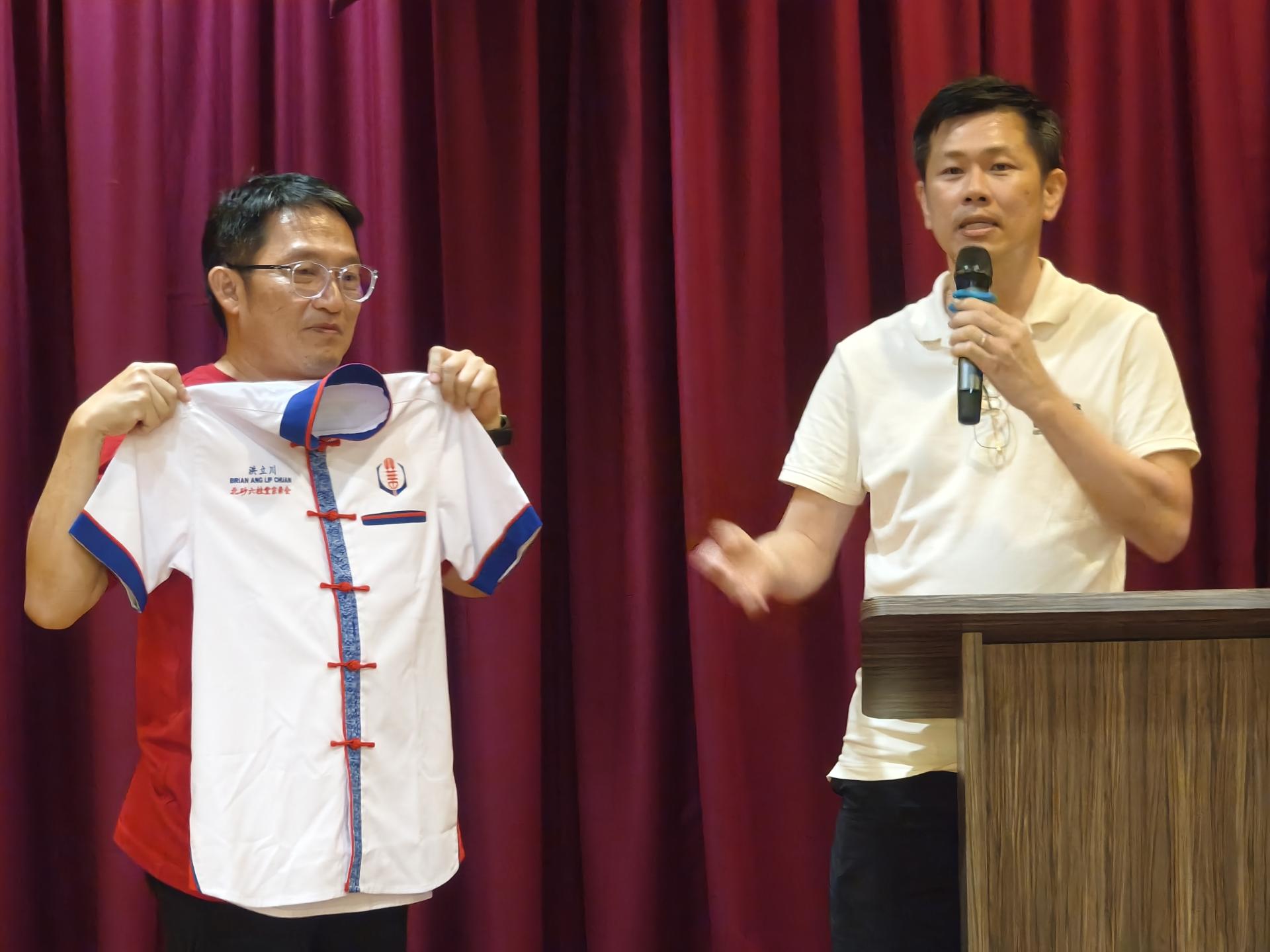 美里省华总会长许信隆（右）在交流会上致词，展示融入中华与婆罗洲文化元素的新届理事制服设计。左为秘书长洪立川。